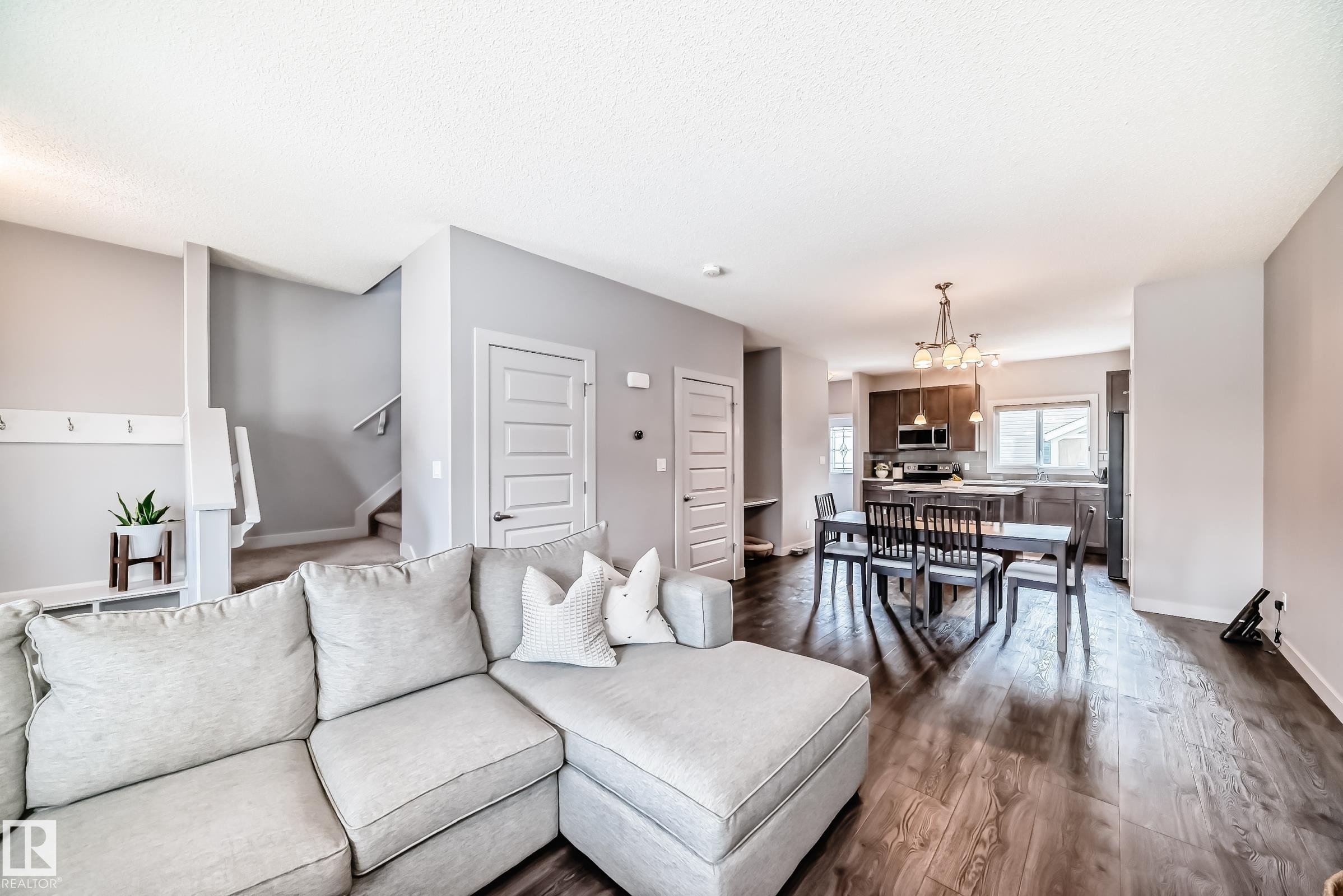 Open-concept living area featuring wood-finish flooring, a contemporary kitchen with dark wood cabinetry, and a dining area illuminated by a modern chandelier - 6919 Cardinal Wynd, Edmonton, AB - Indoor Photo Showing Living Room