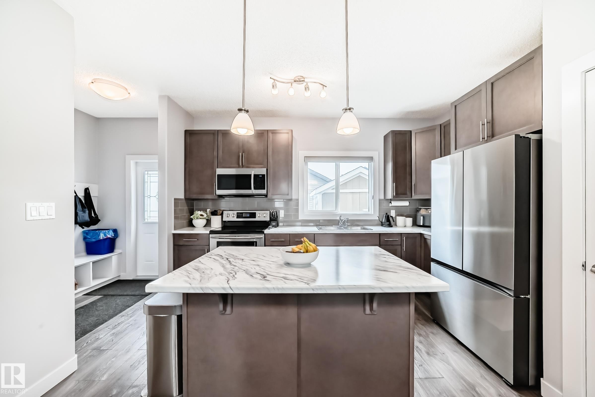 Kitchen featuring a central island, stainless steel appliances, dark wood-finish cabinetry, a tile backsplash, and overhead pendant lighting - 6919 Cardinal Wynd, Edmonton, AB - Indoor Photo Showing Kitchen With Stainless Steel Kitchen