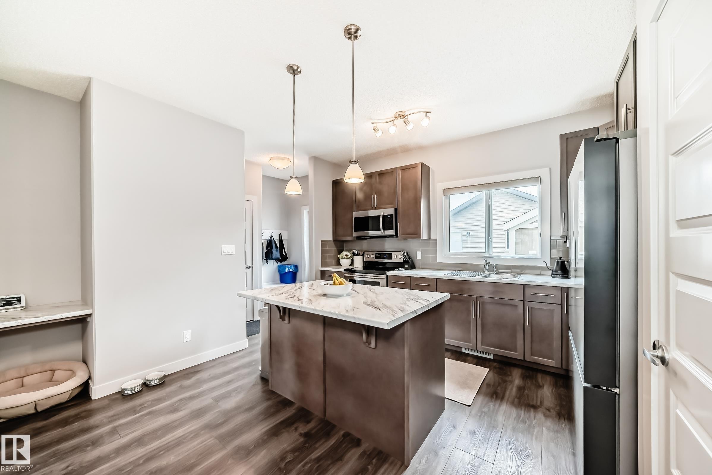 Kitchen featuring a central island, wood-finish flooring, stainless steel appliances, and wood cabinetry - 6919 Cardinal Wynd, Edmonton, AB - Indoor Photo Showing Kitchen