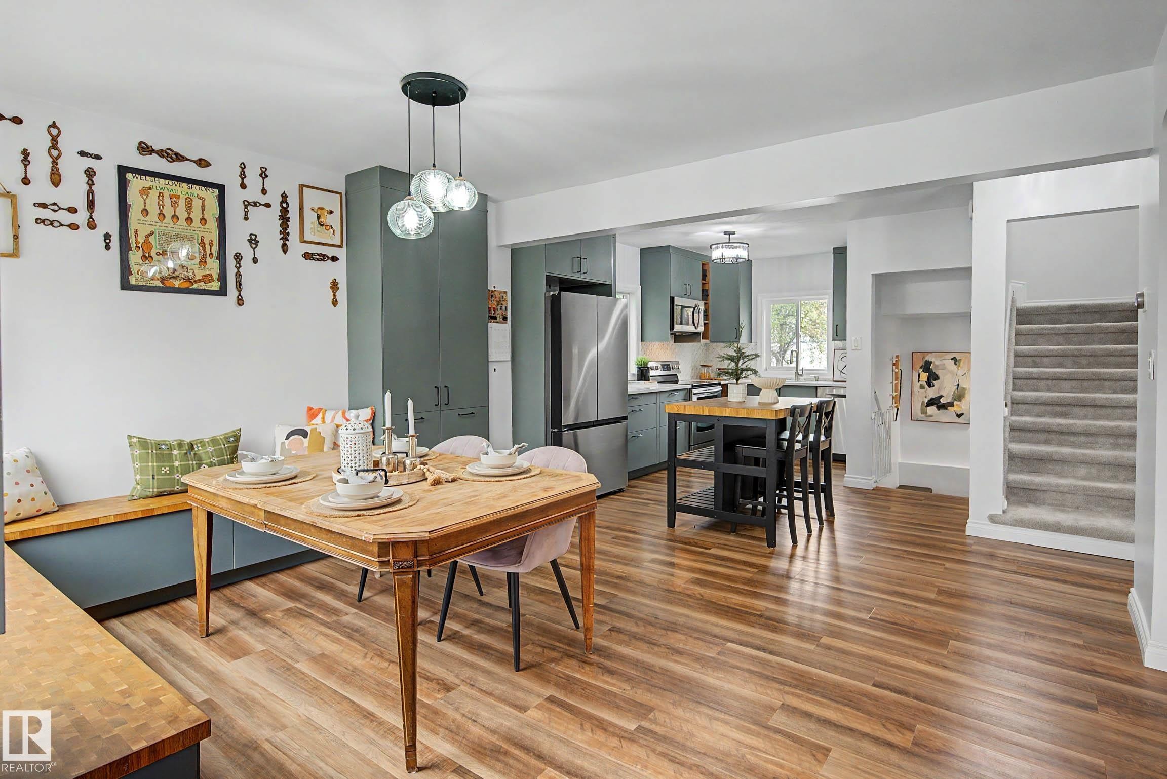 Open-concept dining area featuring wood-finish flooring, a built-in bench with a butcher block top, and a modern three-globe pendant light - 13316 109A Avenue, Edmonton, AB - Indoor Photo Showing Dining Room
