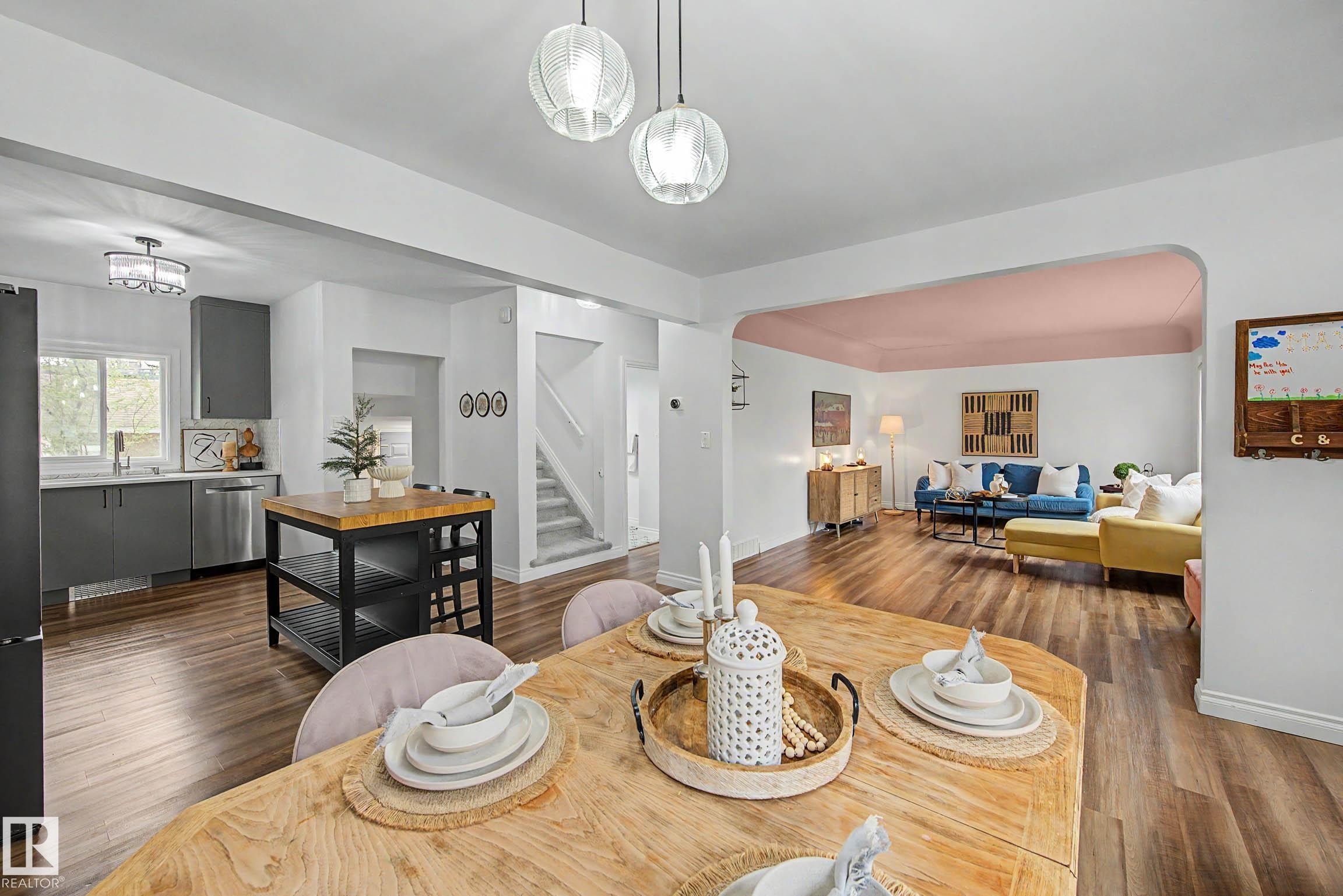 Open-concept living area featuring wood-finish flooring, a kitchen with grey cabinetry and stainless steel appliances, a central kitchen island with a butcher block top, and a dining area with a light wood table - 13316 109A Avenue, Edmonton, AB - Indoor Photo Showing Dining Room