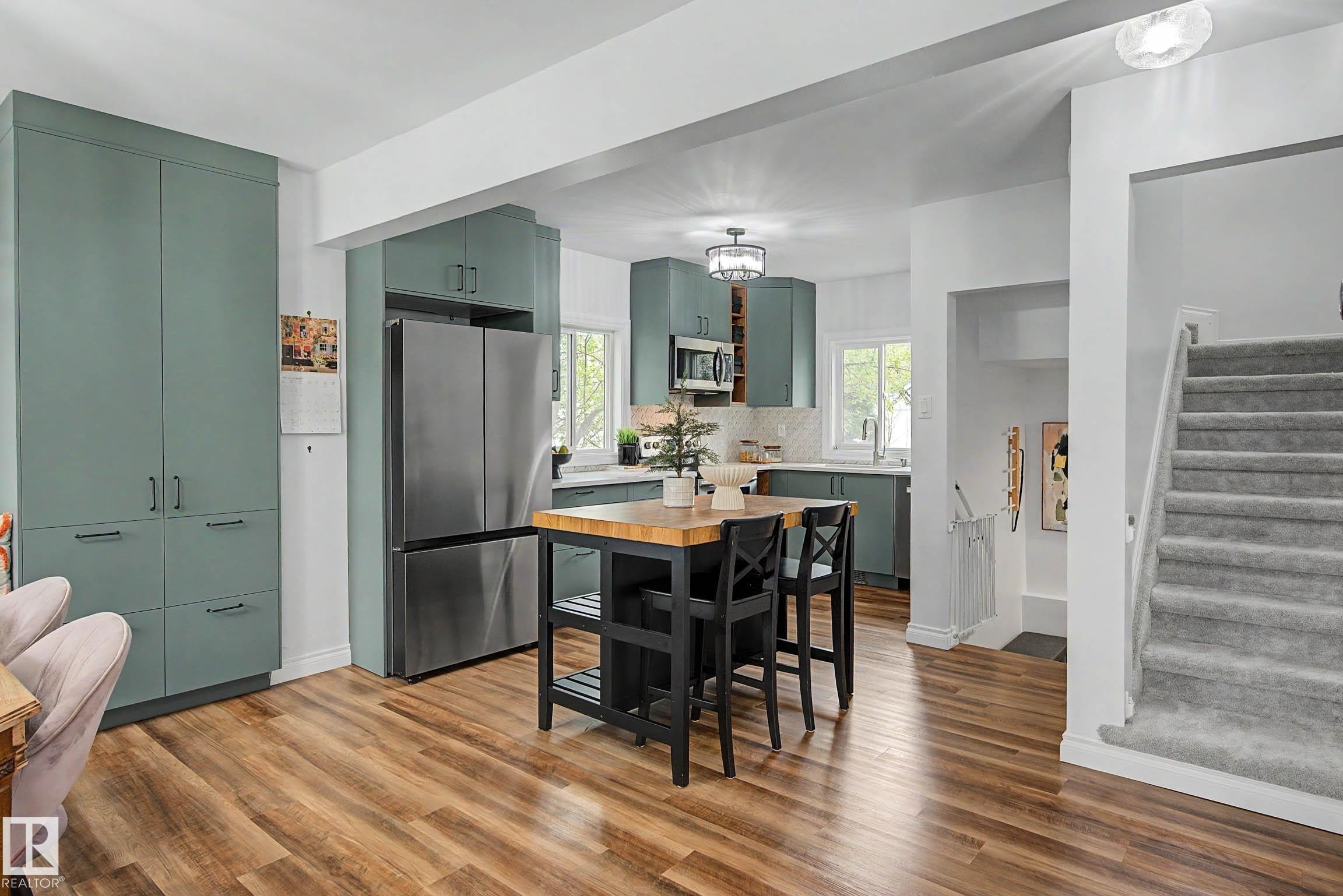 Open-concept kitchen featuring teal cabinetry, stainless steel appliances, a central island with wood countertop, and wood-finish flooring - 13316 109A Avenue, Edmonton, AB - Indoor