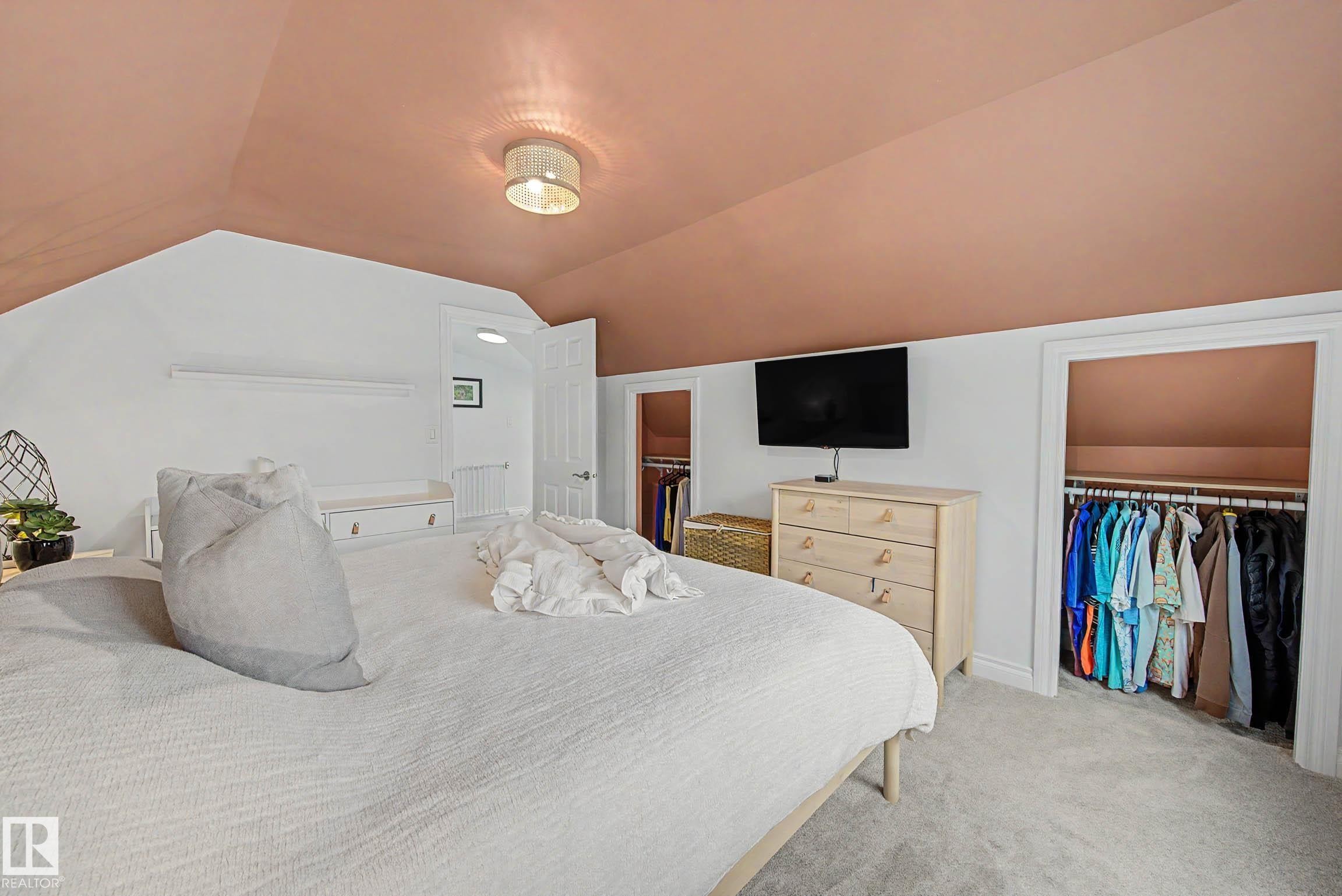 Carpeted room featuring a sloped ceiling, built-in shelving, and two recessed wardrobe areas - 13316 109A Avenue, Edmonton, AB - Indoor Photo Showing Bedroom