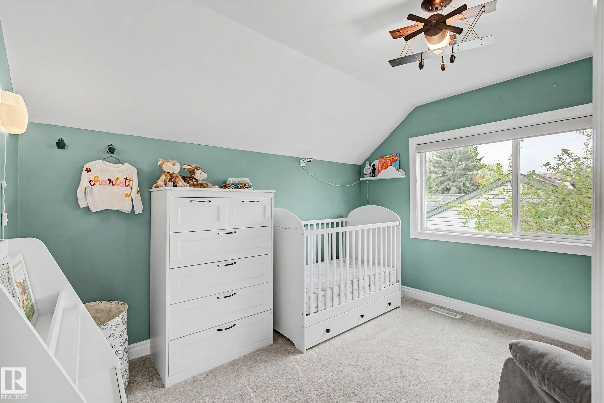 Carpeted room featuring a large window with white trim, sloped ceiling, and a ceiling-mounted light fixture - 13316 109A Avenue, Edmonton, AB - Indoor Photo Showing Bedroom
