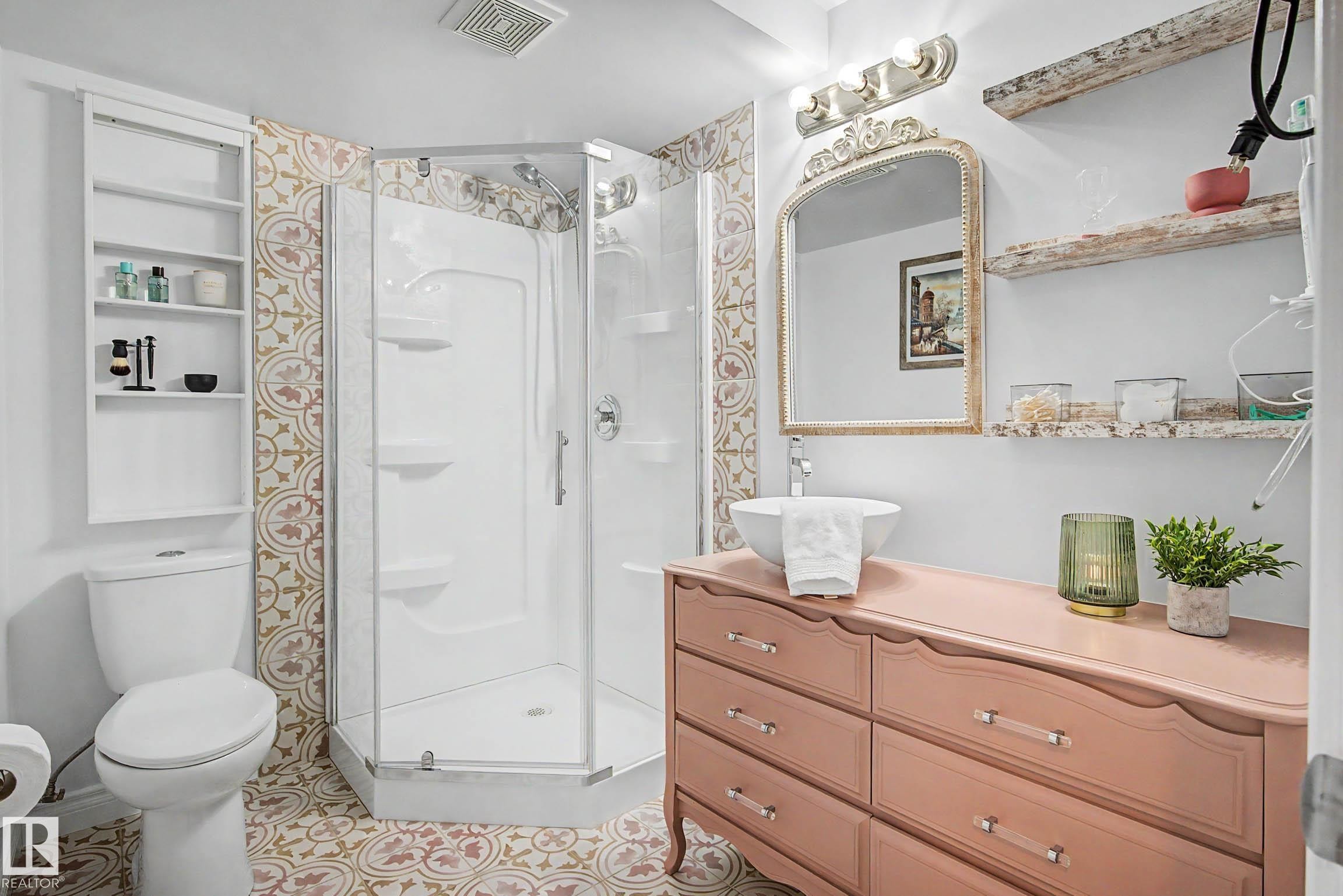 Bathroom featuring a corner shower enclosure, patterned floor and wall tile, a white toilet with built-in shelving, a vanity with a vessel sink, and a decorative mirror - 13316 109A Avenue, Edmonton, AB - Indoor Photo Showing Bathroom