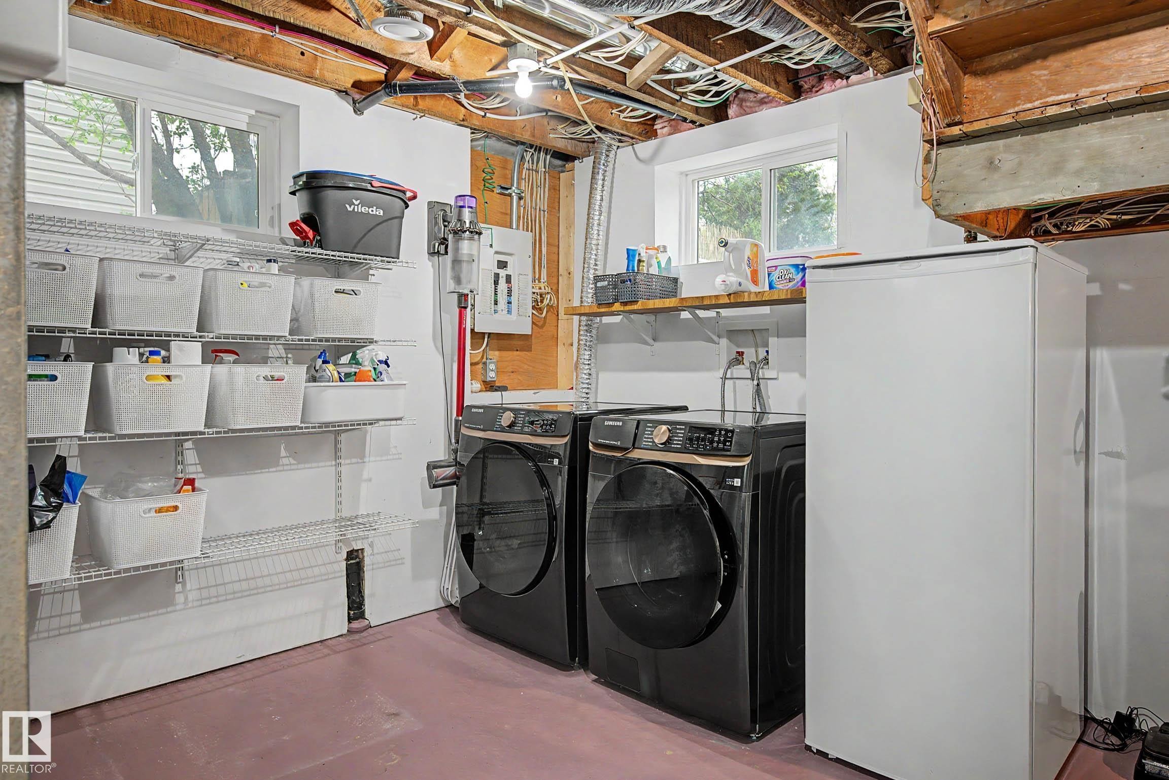 Dedicated laundry area featuring a washer and dryer, ample wire shelving, an additional freestanding freezer, and overhead ceiling joists - 13316 109A Avenue, Edmonton, AB - Indoor Photo Showing Laundry Room