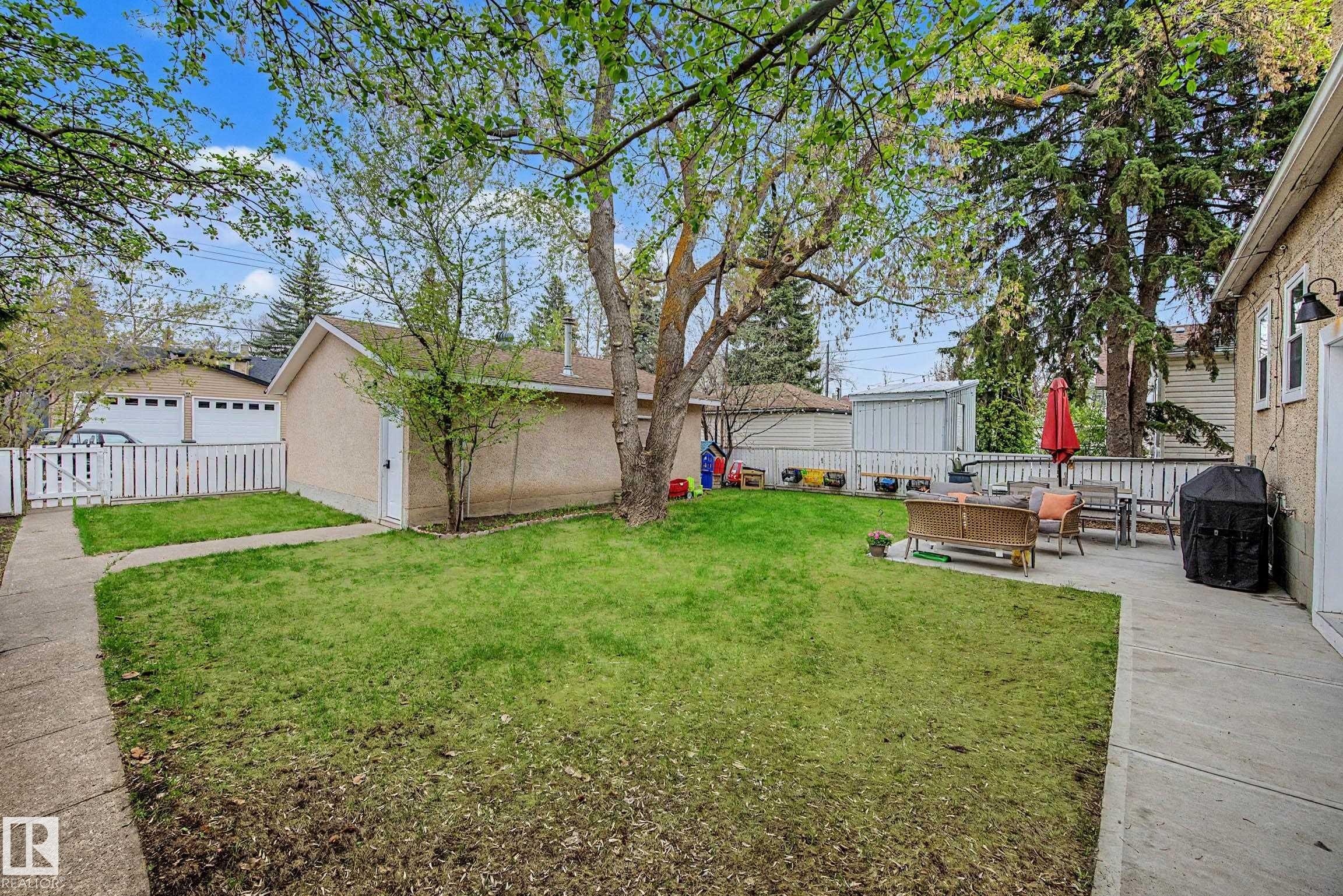 Spacious rear yard featuring an expansive lawn, mature trees, and a concrete patio - 13316 109A Avenue, Edmonton, AB - Outdoor