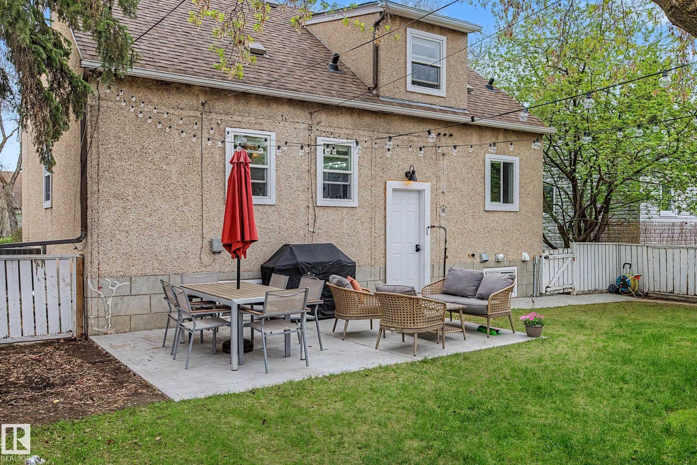 Rear exterior featuring a concrete patio, expansive lawn, and white privacy fencing - 13316 109A Avenue, Edmonton, AB - Outdoor With Exterior