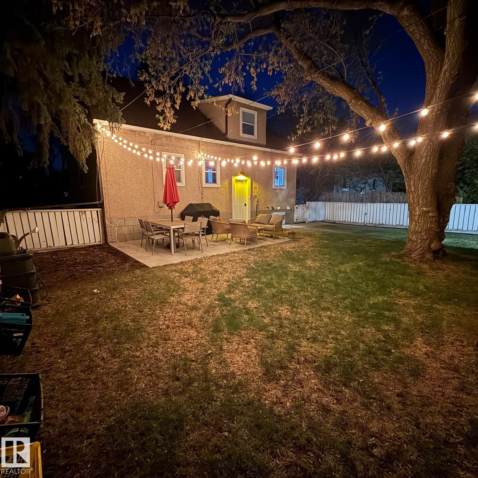 Expansive backyard featuring a concrete patio, string lighting, and a white privacy fence - 13316 109A Avenue, Edmonton, AB - Outdoor