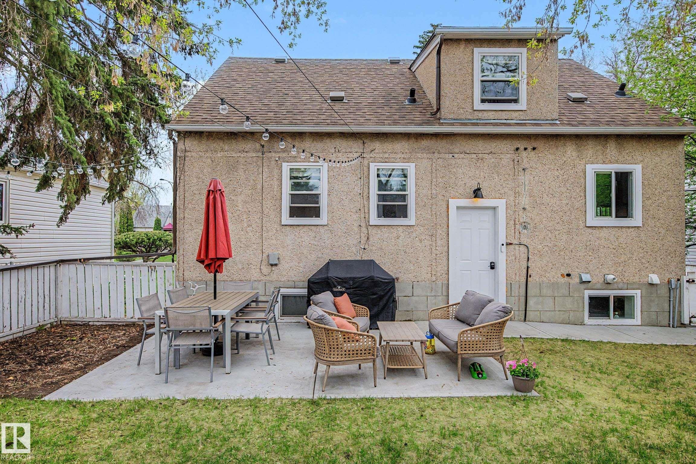 Rear exterior featuring a concrete patio, shingle roof, dormer window, lower-level windows, and a white rear entry door - 13316 109A Avenue, Edmonton, AB - Outdoor With Exterior