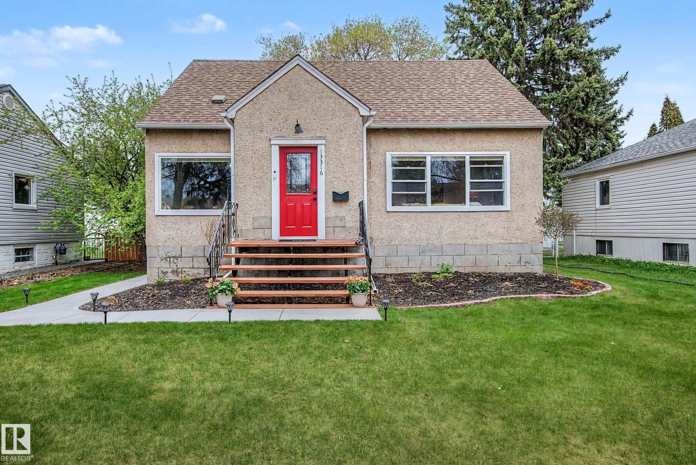Stucco exterior featuring a prominent red entry door, natural wood steps with a metal handrail, white window frames, and a shingle roof - 13316 109A Avenue, Edmonton, AB - Outdoor