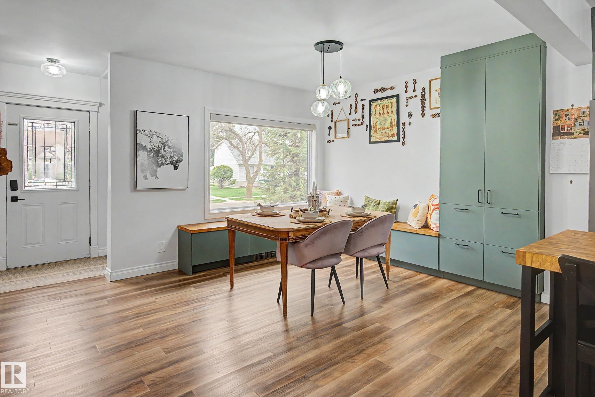 Open-concept dining area featuring wood-finish flooring, a large window, built-in bench seating, and expansive cabinetry - 13316 109A Avenue, Edmonton, AB - Indoor Photo Showing Dining Room
