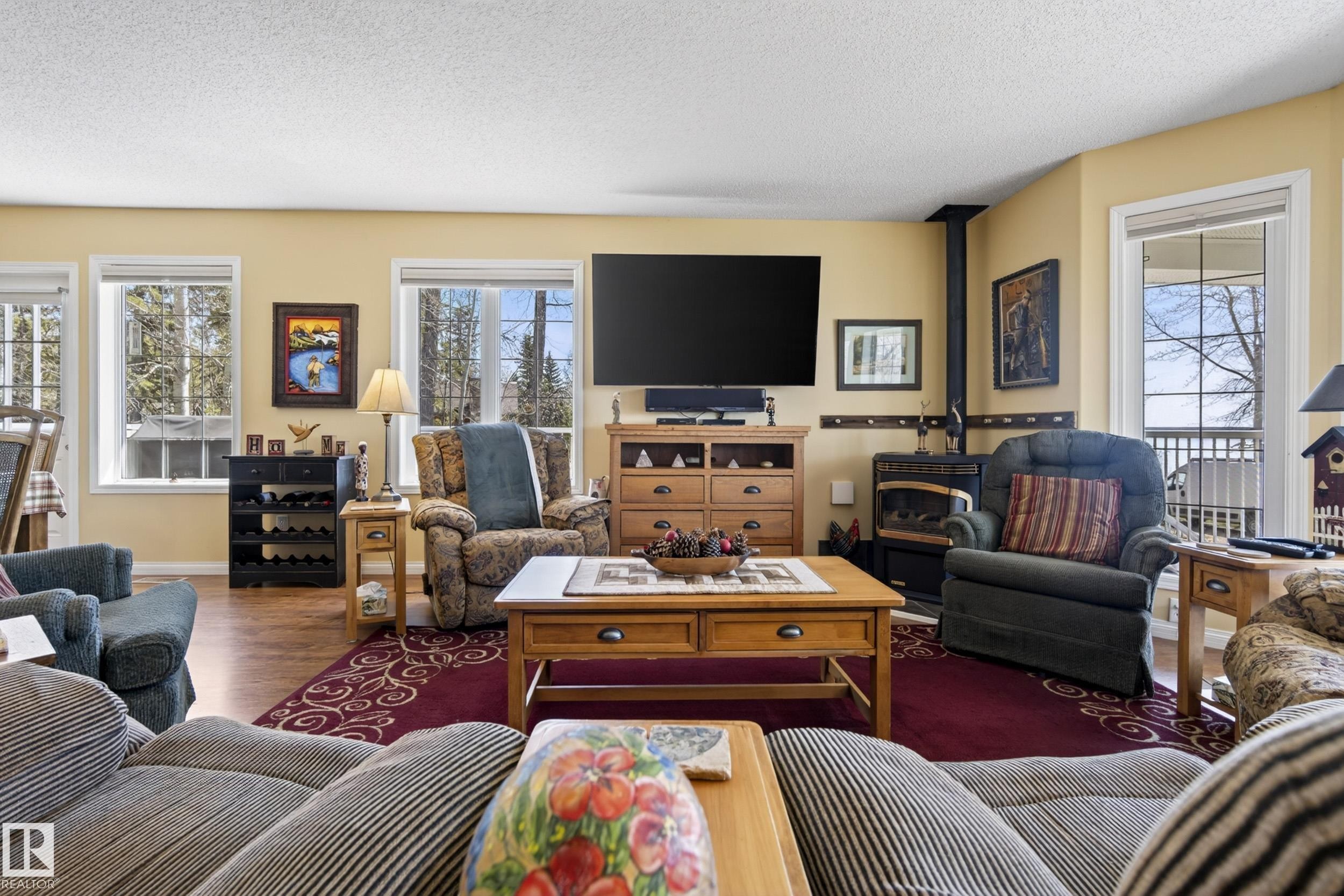Spacious living area featuring wood-finish flooring, multiple large windows, and a built-in wood-burning stove - 77 Lakeshore Drive, Rural Leduc County, AB - Indoor Photo Showing Living Room