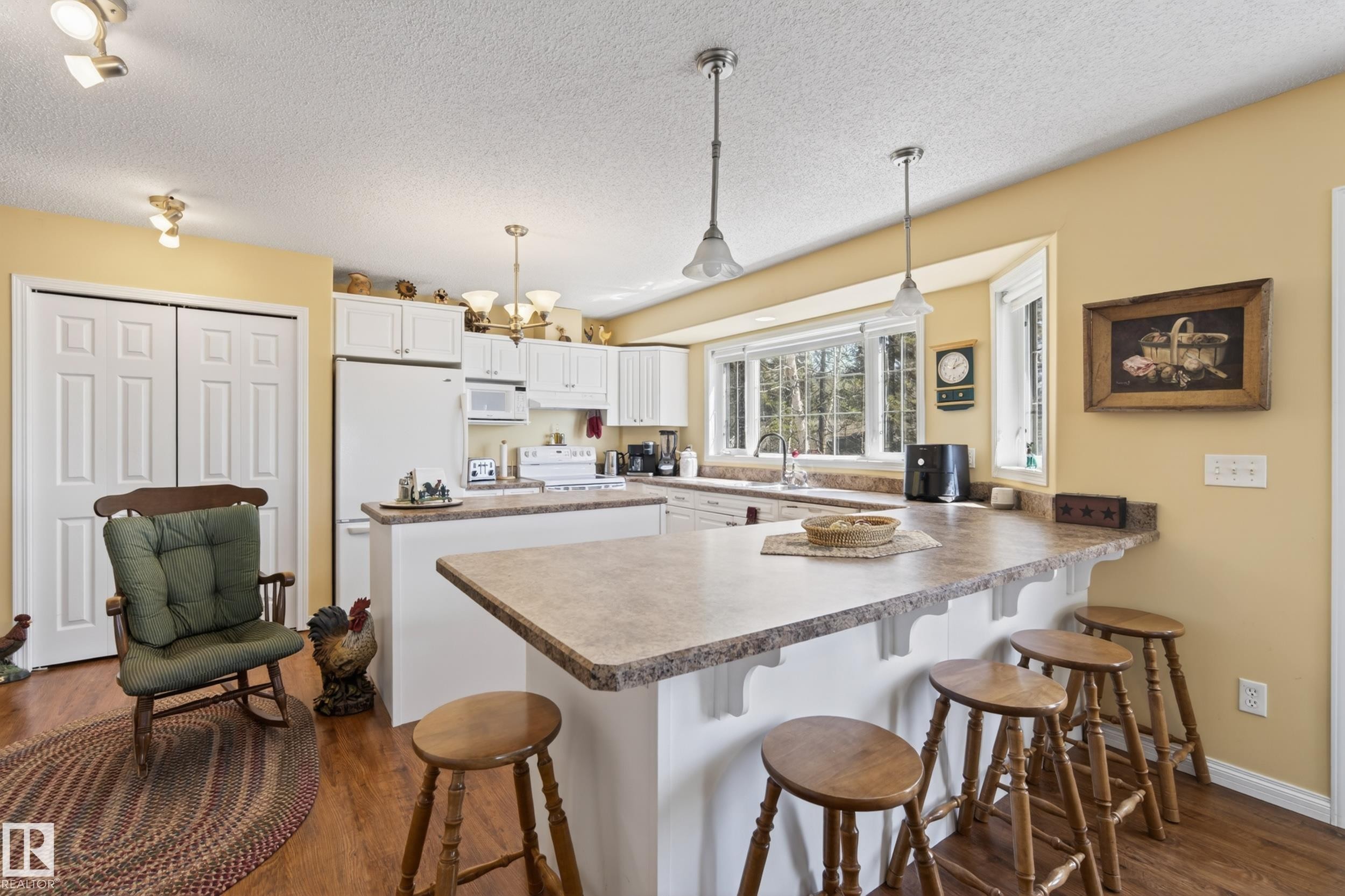 Kitchen with white cabinetry, wood-finish flooring, and a breakfast bar - 77 Lakeshore Drive, Rural Leduc County, AB - Indoor