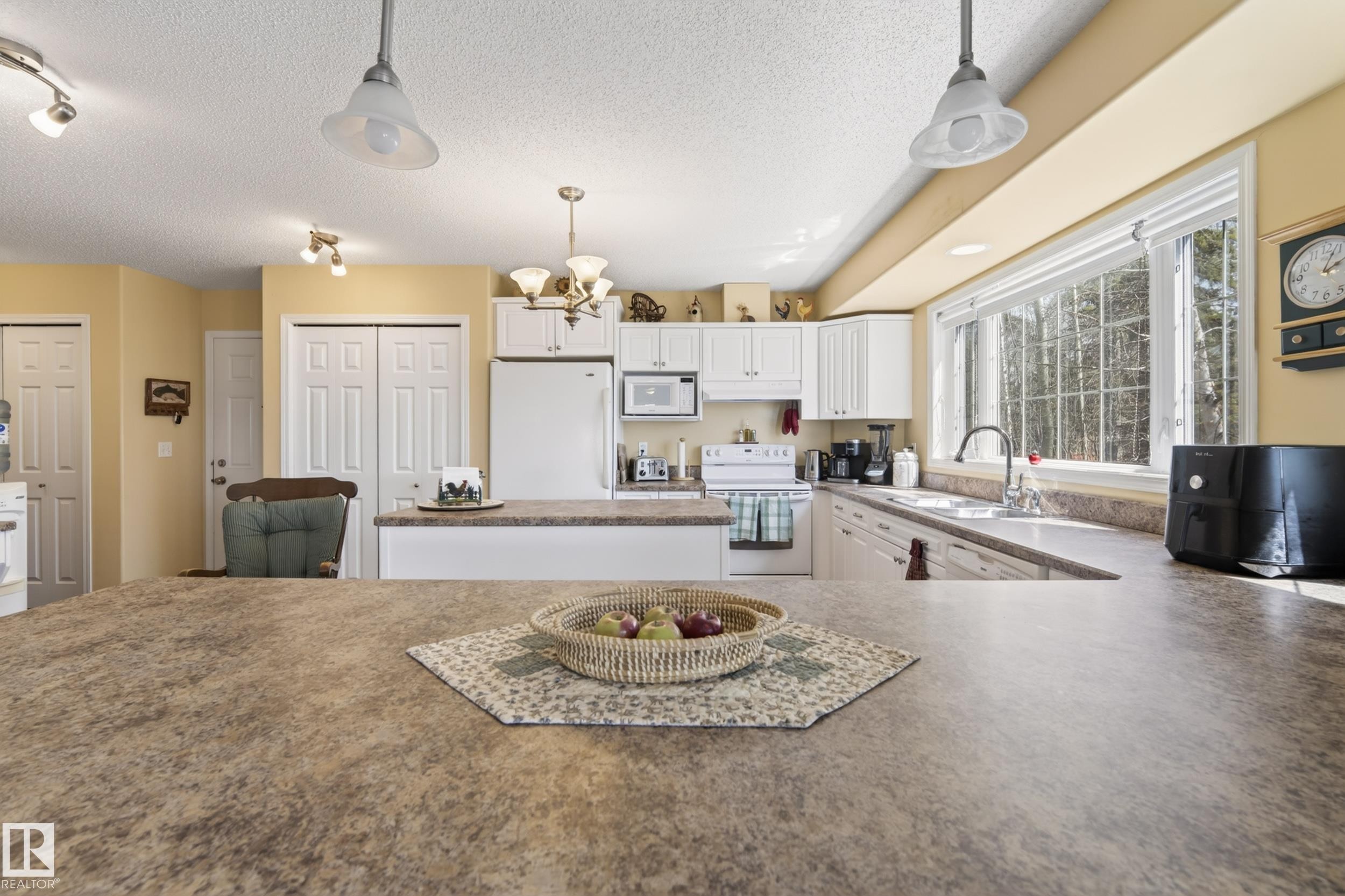 Kitchen featuring white cabinetry, a large center island with a stone-finish countertop, and a window overlooking a wooded area - 77 Lakeshore Drive, Rural Leduc County, AB - Indoor Photo Showing Kitchen