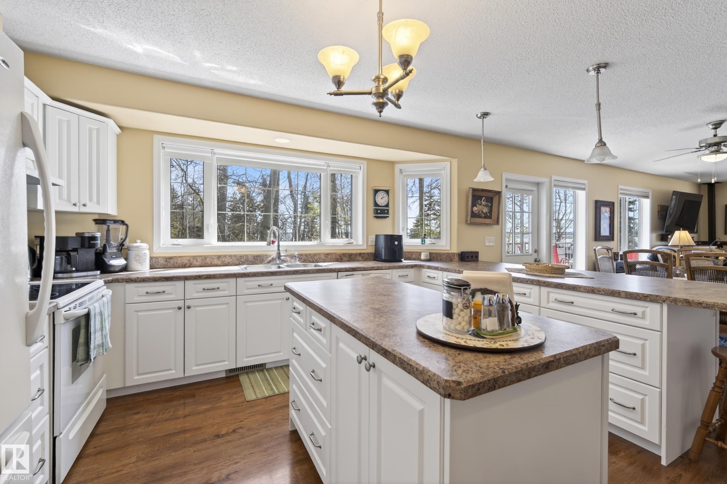 Bright kitchen featuring white cabinetry, wood-finish flooring, a central island, and multiple windows - 77 Lakeshore Drive, Rural Leduc County, AB - Indoor Photo Showing Kitchen