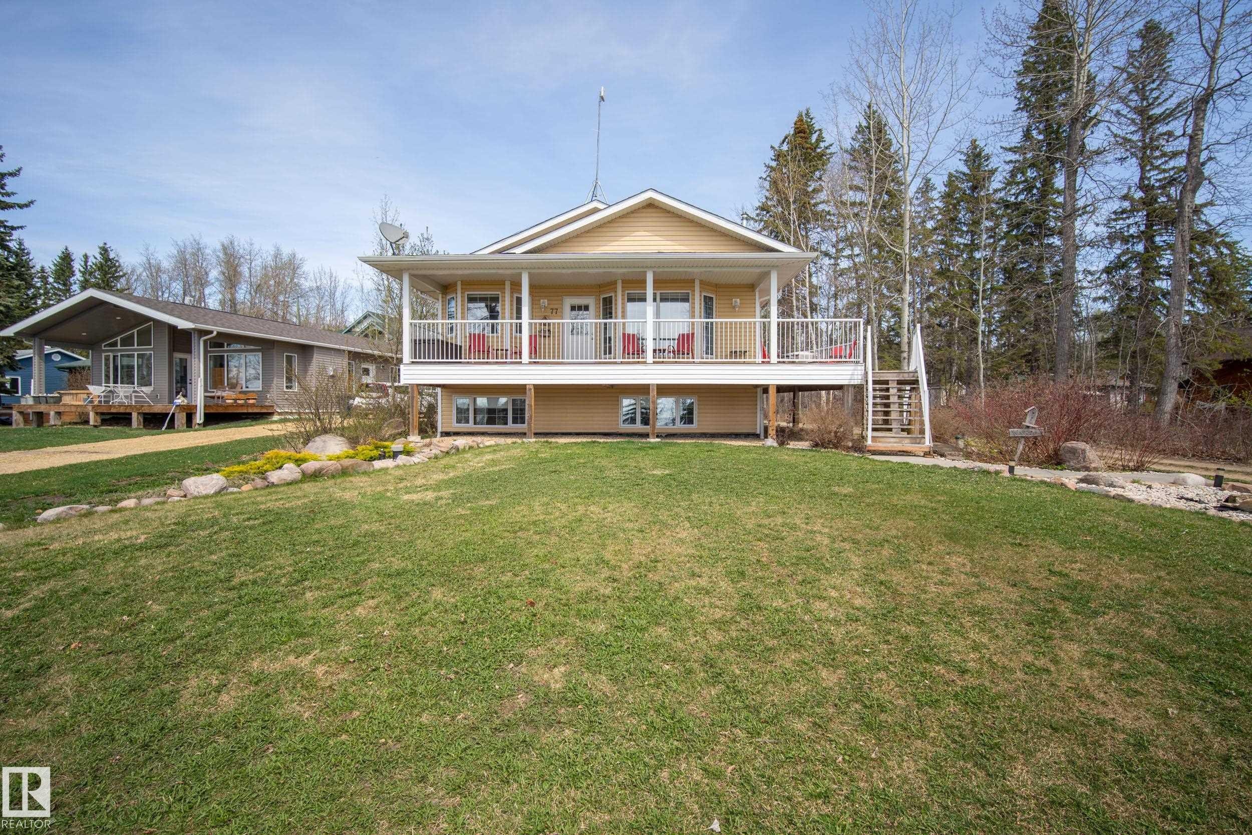 Elevated yellow-sided residence featuring a covered front porch with white railings - 77 Lakeshore Drive, Rural Leduc County, AB - Outdoor With Deck Patio Veranda