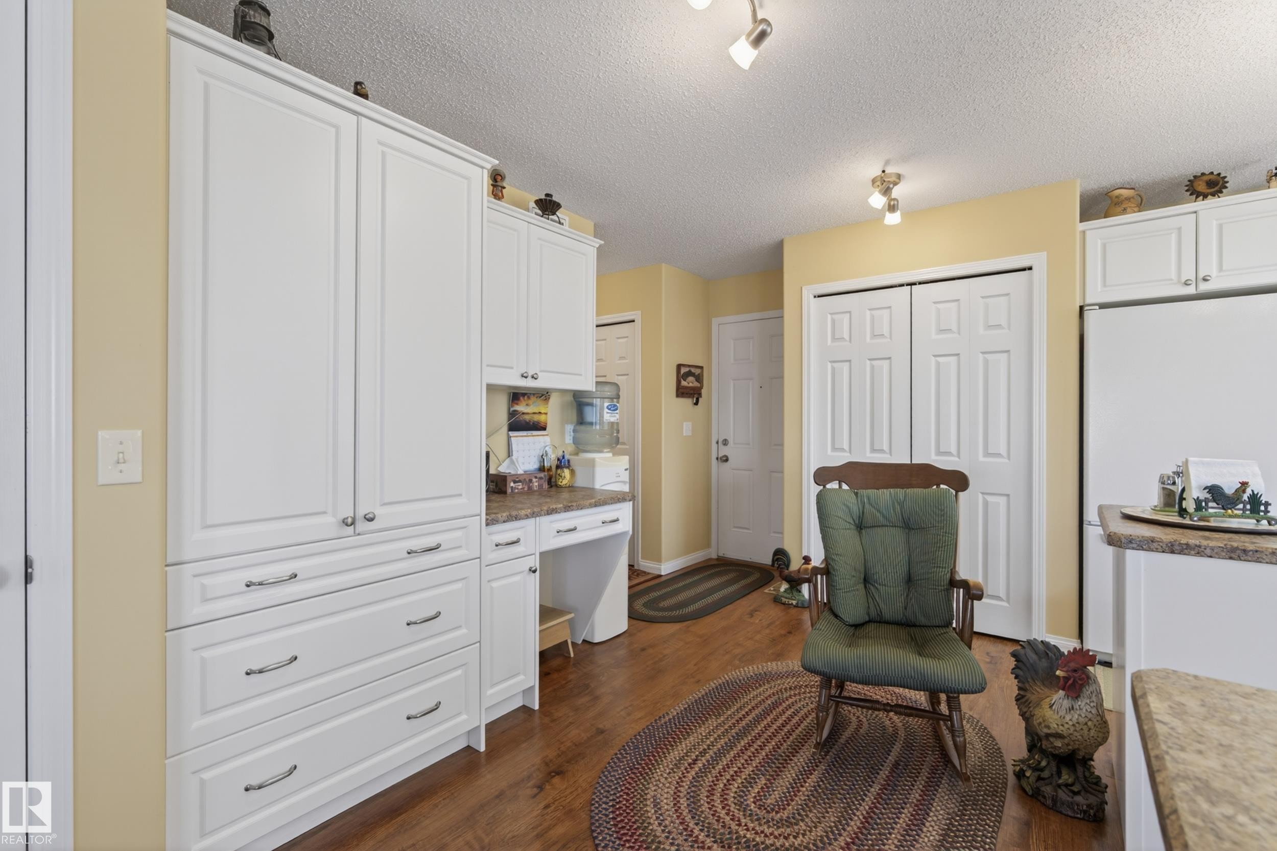 Kitchen area featuring white cabinetry, wood-finish flooring, a built-in desk, track lighting, and a white refrigerator - 77 Lakeshore Drive, Rural Leduc County, AB - Indoor