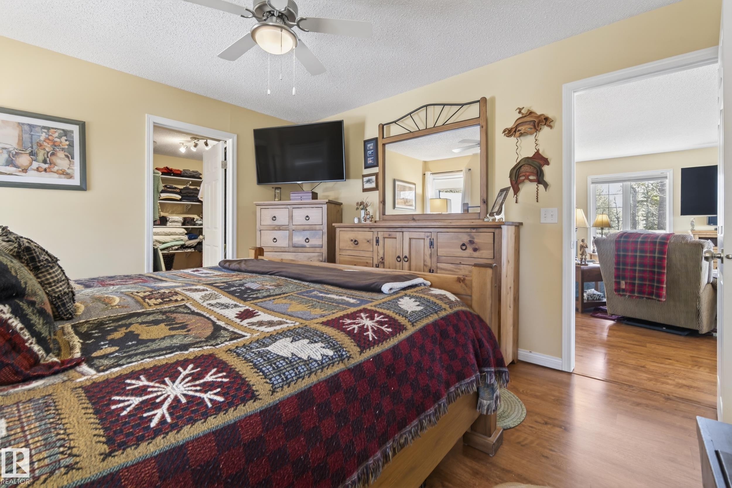 Bedroom featuring a ceiling fan with integrated lighting, a walk-in closet, and a doorway opening to an additional room with wood-finish flooring and a window - 77 Lakeshore Drive, Rural Leduc County, AB - Indoor Photo Showing Bedroom