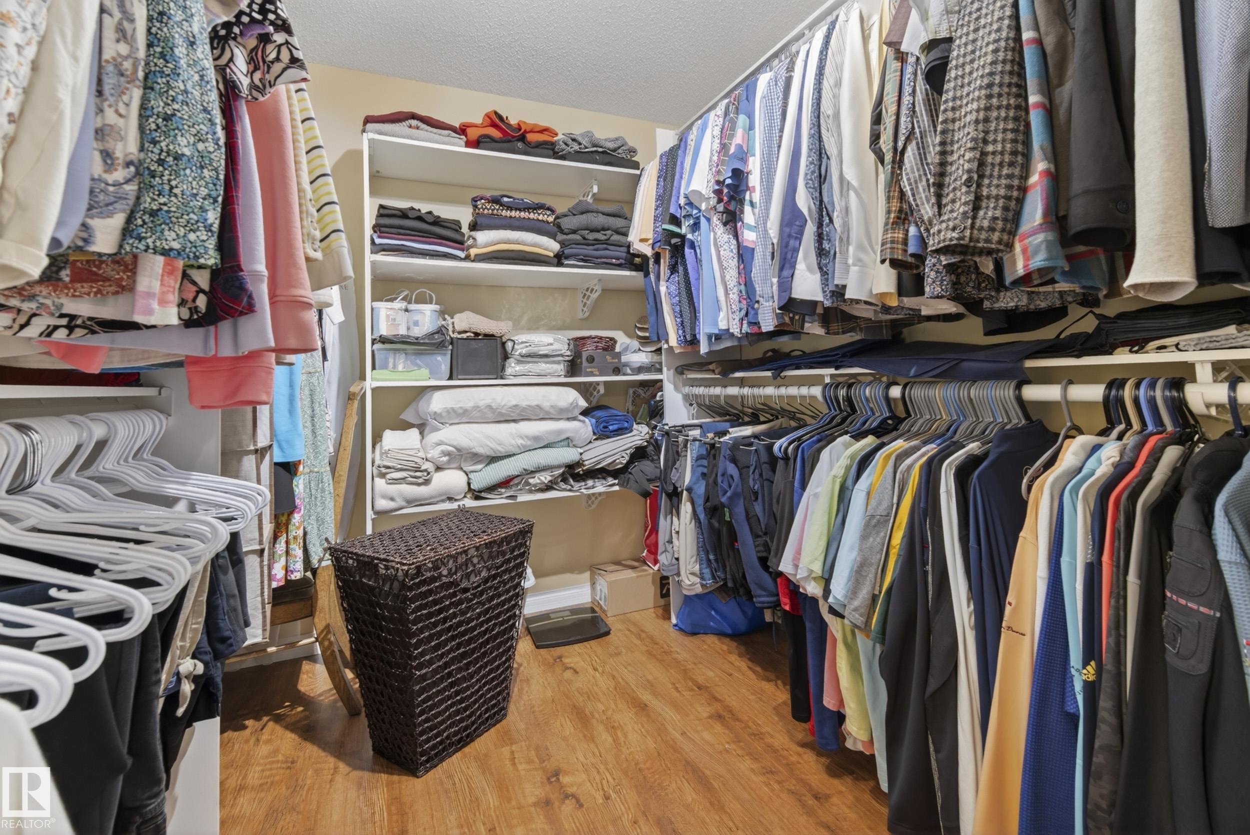 Walk-in closet featuring wood-finish flooring, white built-in shelving, and multiple clothing rods for extensive storage - 77 Lakeshore Drive, Rural Leduc County, AB - Indoor With Storage
