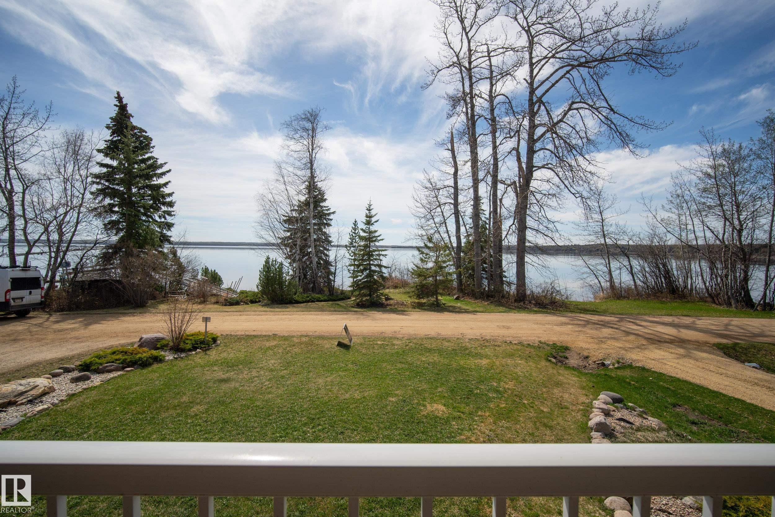 Expansive property featuring a large body of water, mature evergreen trees, lush green lawn, and a white railing - 77 Lakeshore Drive, Rural Leduc County, AB - Outdoor With View