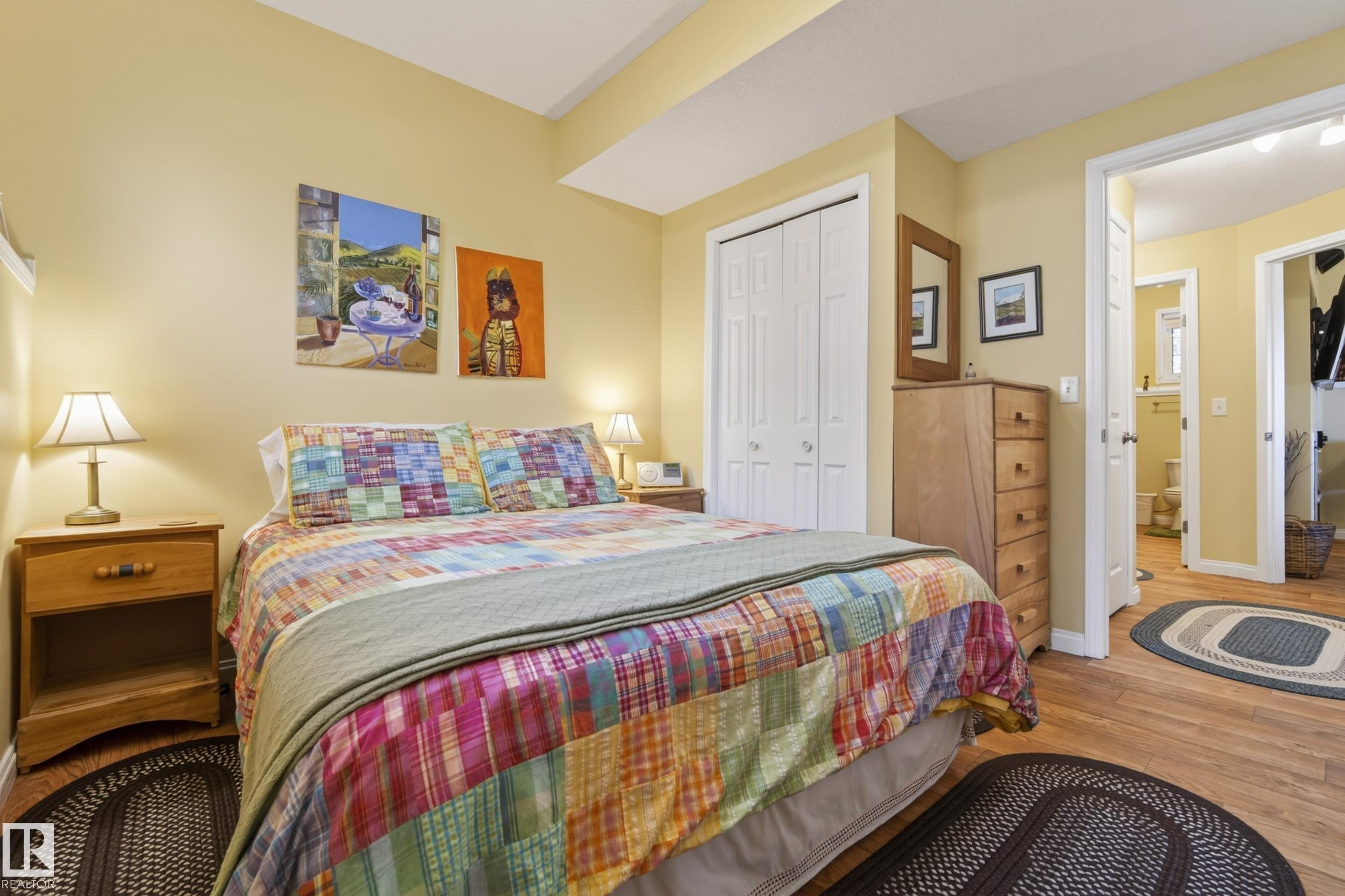 Bedroom featuring wood-finish flooring, a bi-fold door closet, and a doorway opening to an additional room with a white toilet - 77 Lakeshore Drive, Rural Leduc County, AB - Indoor Photo Showing Bedroom