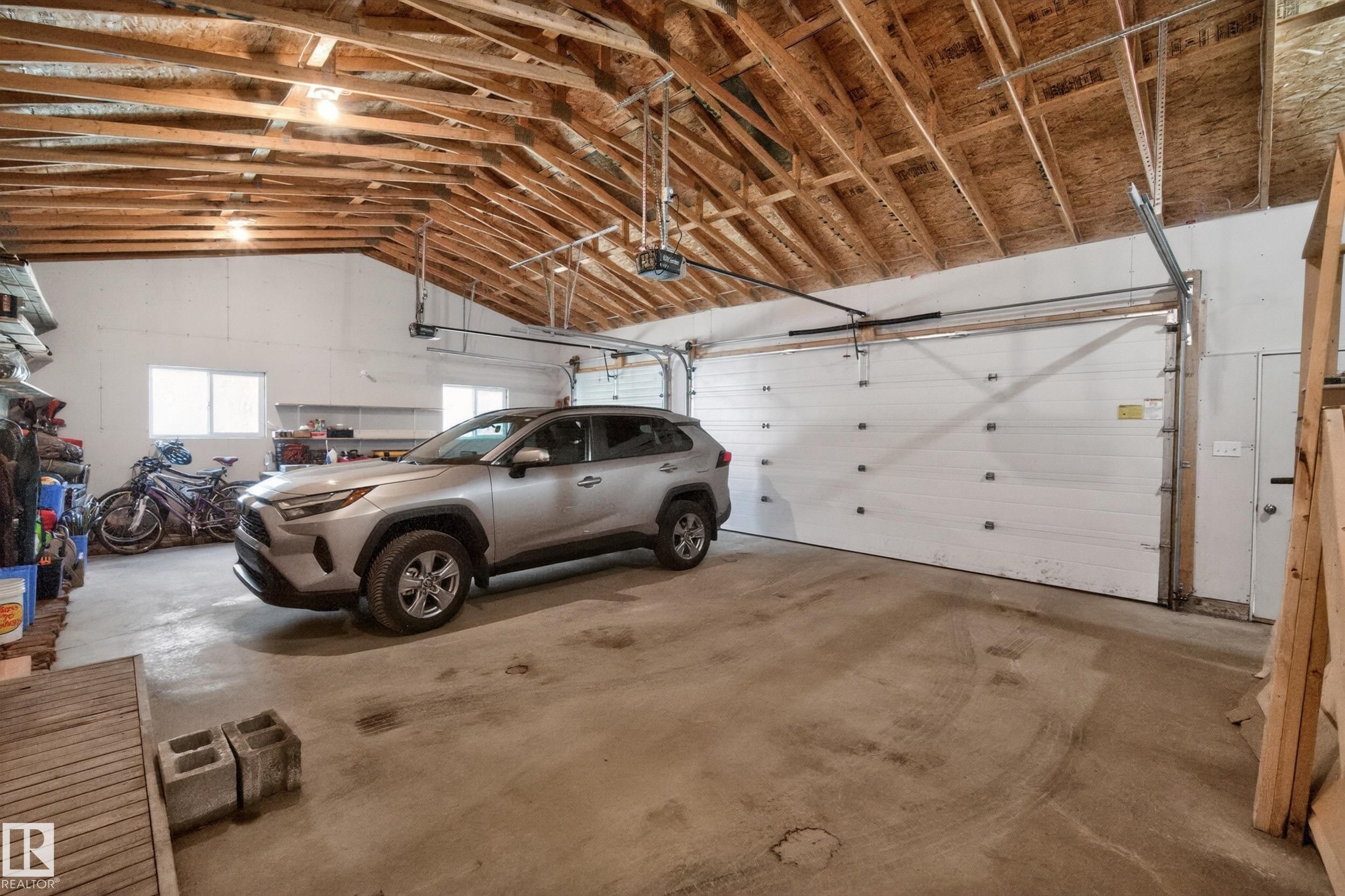 Spacious garage featuring a concrete floor, exposed wood beam ceiling, two automatic garage doors, and multiple windows for natural light - 77 Lakeshore Drive, Rural Leduc County, AB - Indoor Photo Showing Garage