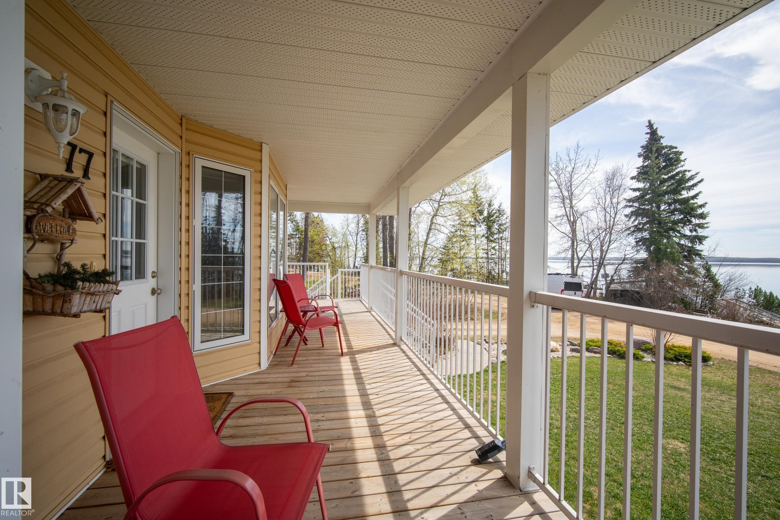 Covered wood-finish porch with white railing, featuring a panel door with sidelight and multiple windows - 77 Lakeshore Drive, Rural Leduc County, AB - Outdoor With Deck Patio Veranda With Exterior