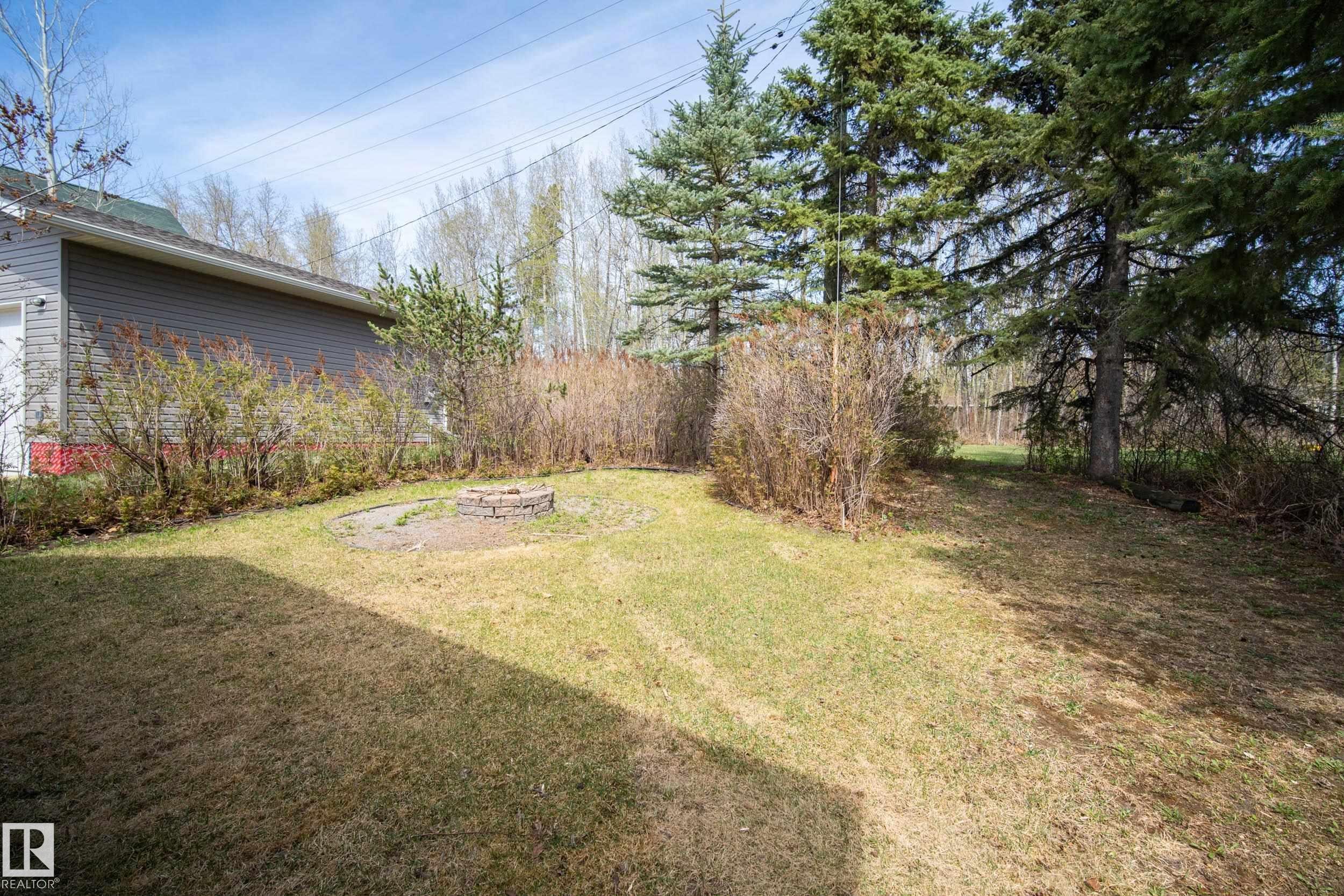 Expansive backyard featuring a stone-ringed fire pit and mature evergreen trees - 77 Lakeshore Drive, Rural Leduc County, AB - Outdoor