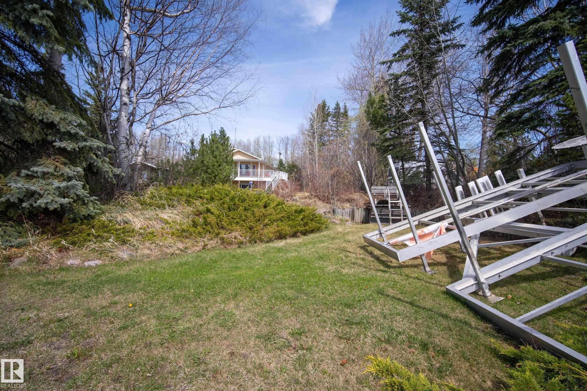 Expansive exterior lot featuring a sloped lawn, mature evergreen trees, and established shrubbery - 77 Lakeshore Drive, Rural Leduc County, AB - Outdoor With View