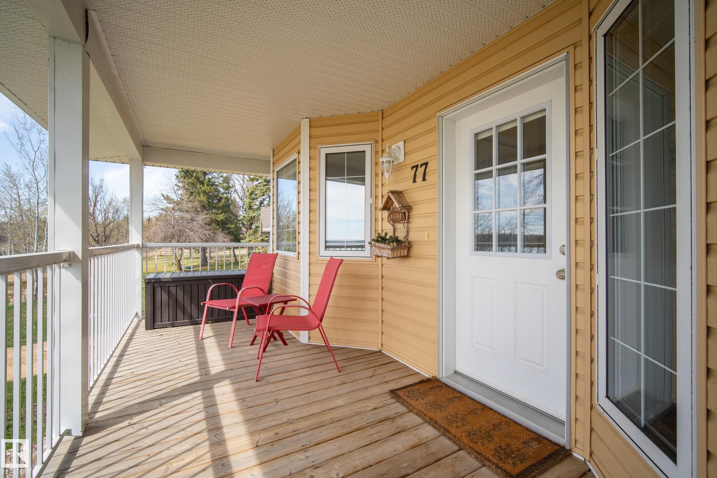 Covered porch featuring wood-finish decking, white railings, and siding in a muted yellow tone - 77 Lakeshore Drive, Rural Leduc County, AB - Outdoor With Deck Patio Veranda With Exterior