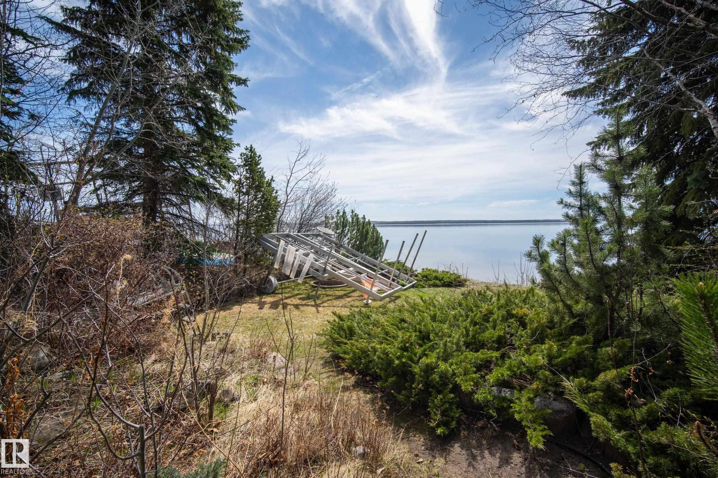 Landscaped grounds featuring mature evergreen trees and low-lying shrubs - 77 Lakeshore Drive, Rural Leduc County, AB - Outdoor With Body Of Water With View