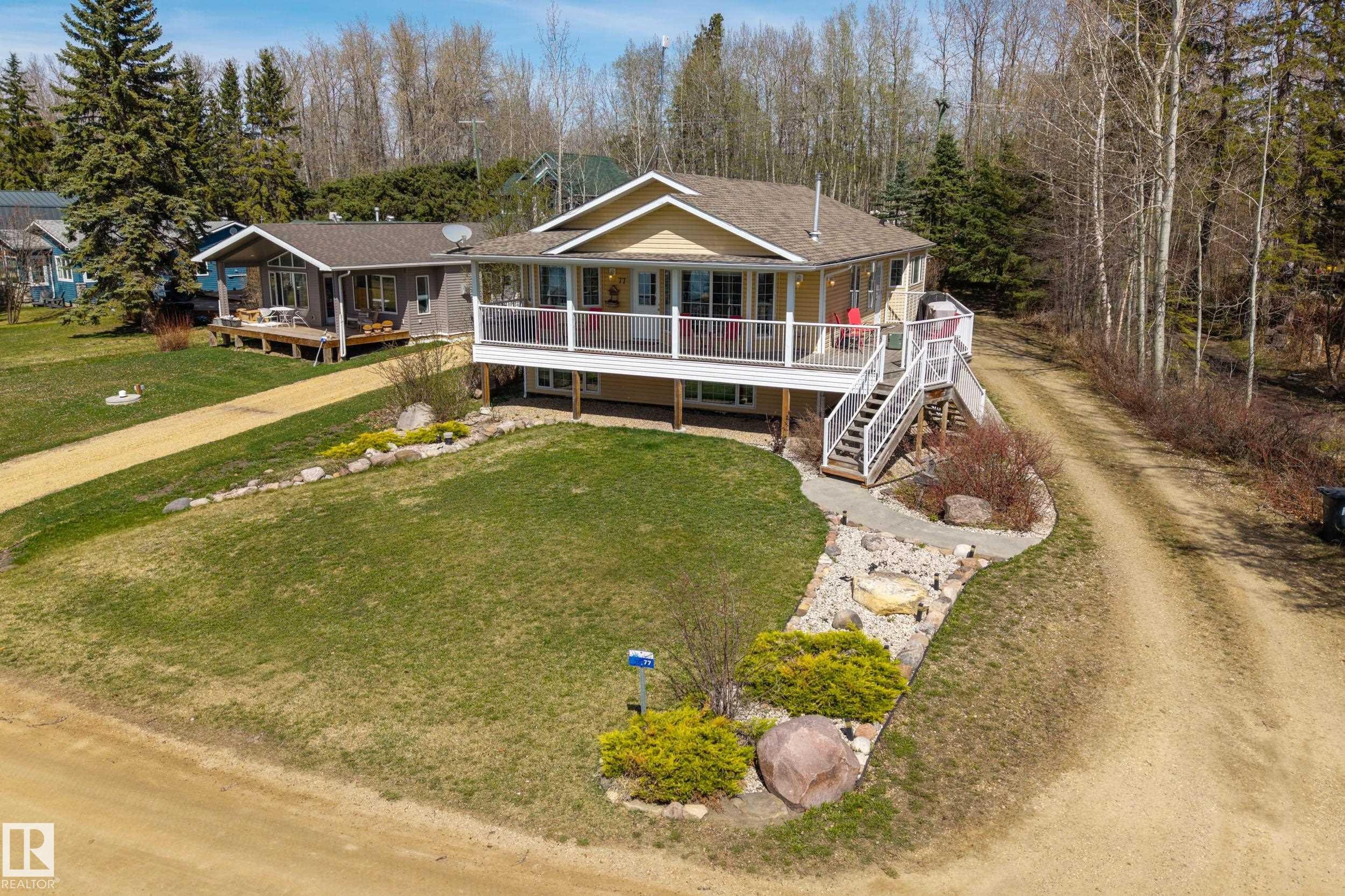 Elevated residence featuring a covered deck with white railings, a multi-level exterior staircase, and a gravel driveway - 77 Lakeshore Drive, Rural Leduc County, AB - Outdoor With Deck Patio Veranda