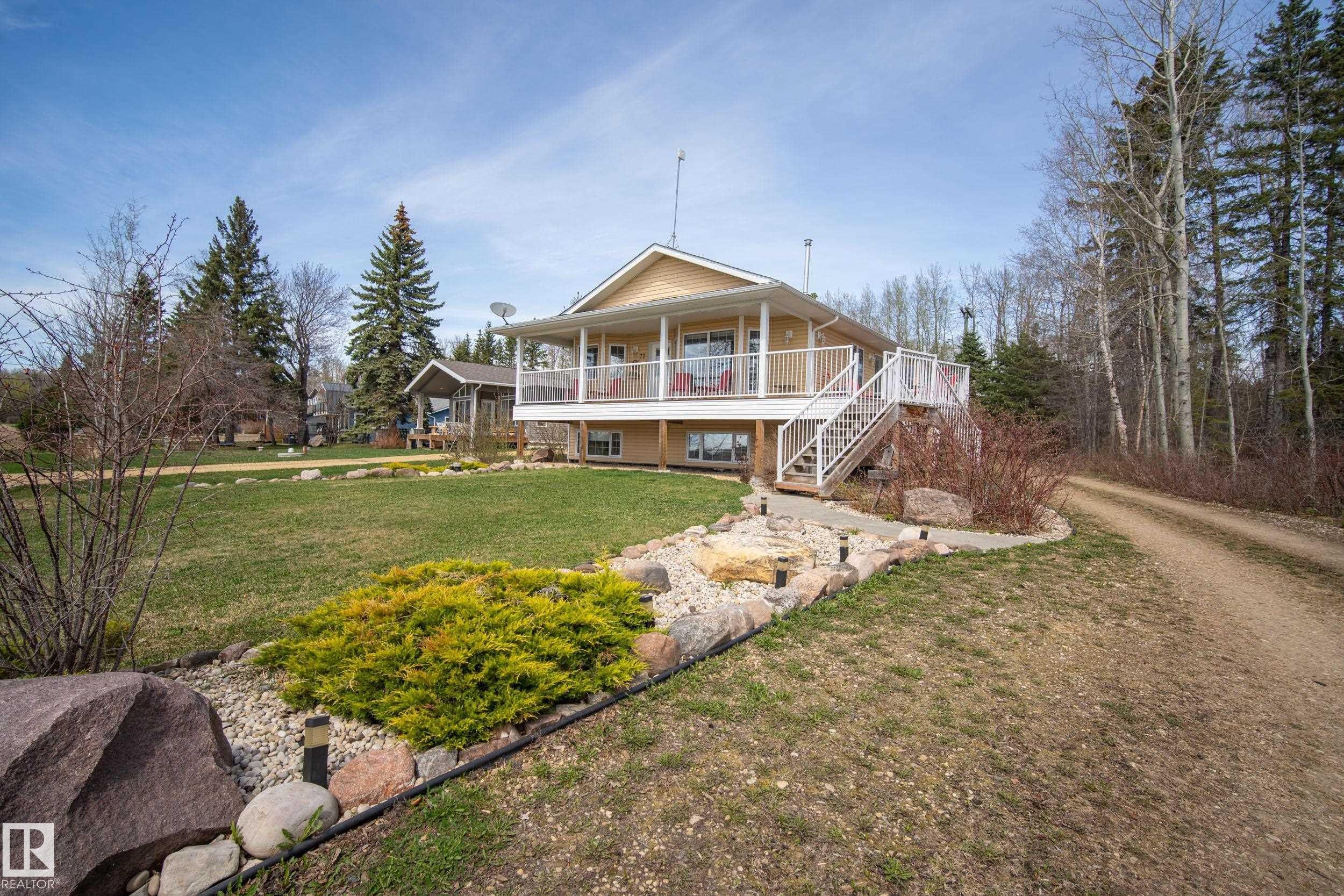Raised home with a large deck, white railings, and an exterior staircase - 77 Lakeshore Drive, Rural Leduc County, AB - Outdoor