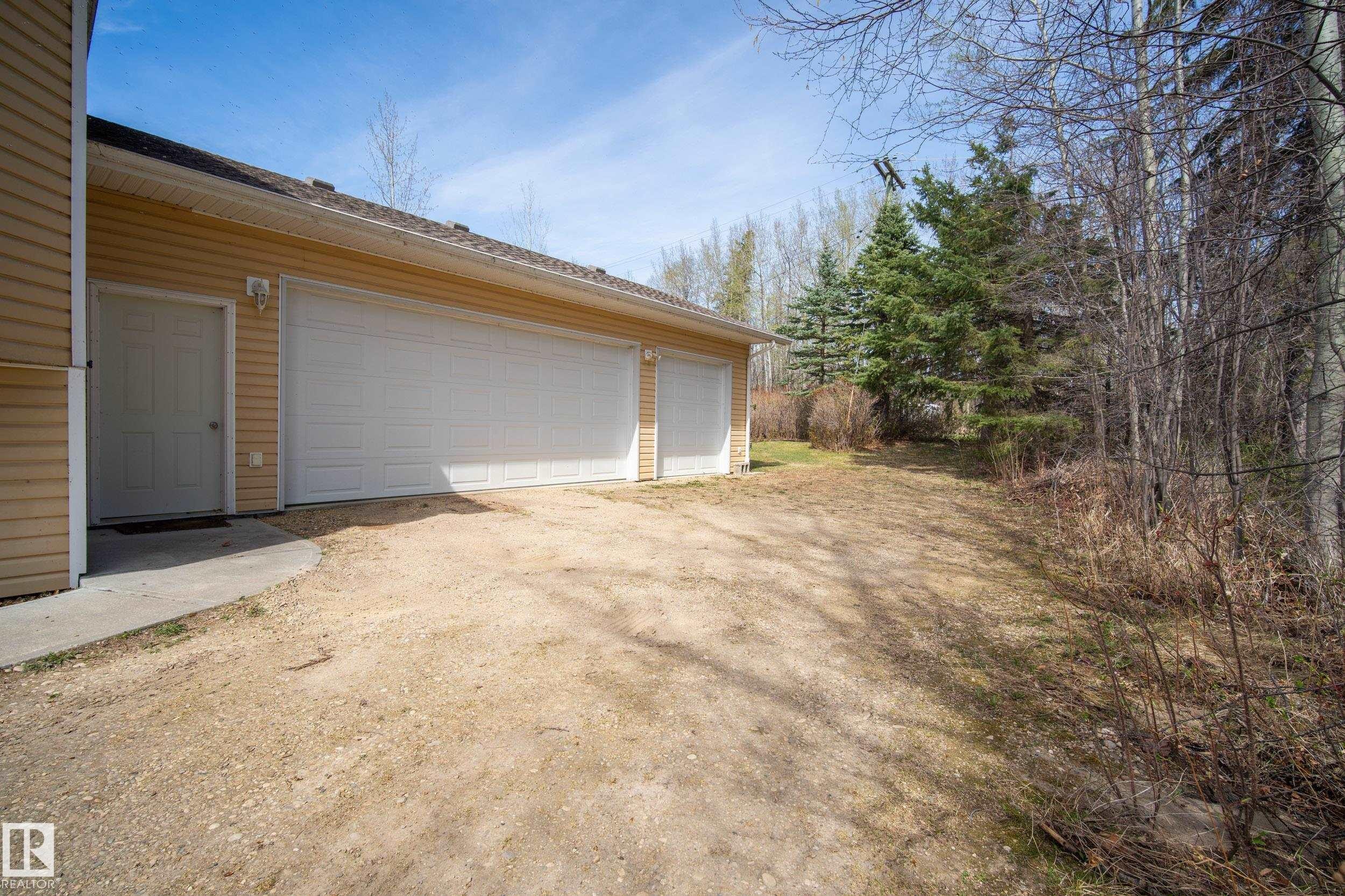 Three-car garage with white paneled doors and tan vinyl siding - 77 Lakeshore Drive, Rural Leduc County, AB - Outdoor With Exterior