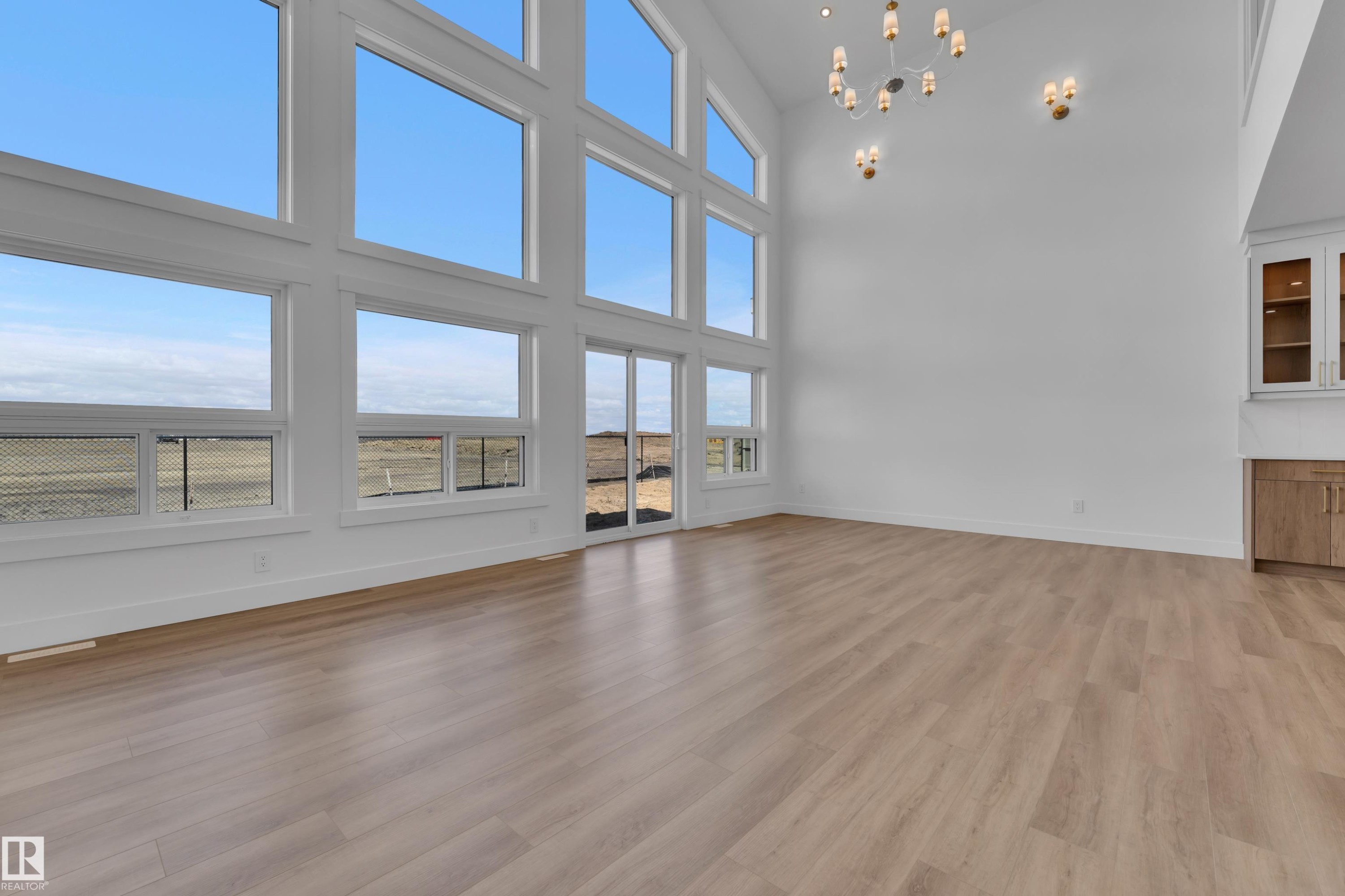 Vaulted ceilings with a statement chandelier, expansive multi-panel windows, wood-finish flooring, sliding glass door access, and built-in cabinetry with glass display fronts - 13128 187 Avenue, Edmonton, AB - Indoor Photo Showing Other Room