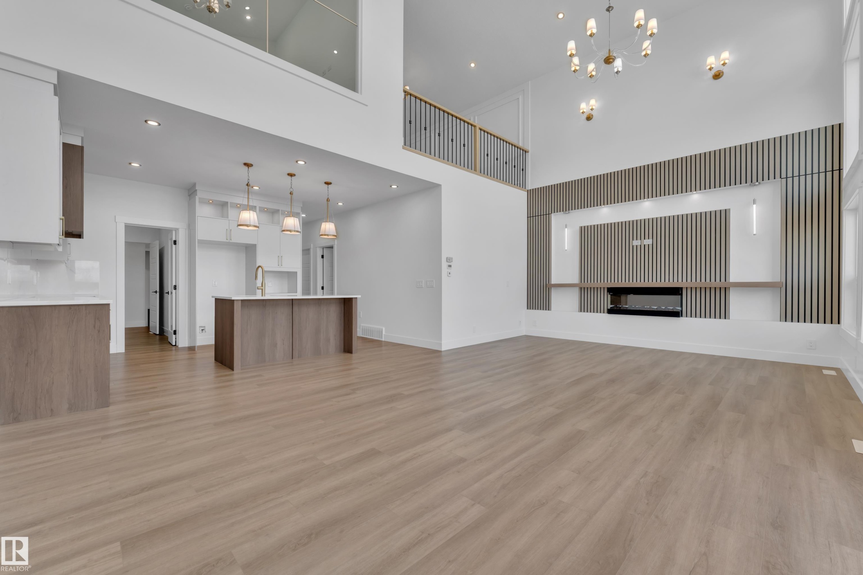 Open-concept living space featuring wood-finish flooring, a contemporary kitchen island with pendant lighting, a two-story accent wall with a linear fireplace, and a second-level balcony with metal railings - 13128 187 Avenue, Edmonton, AB - Indoor