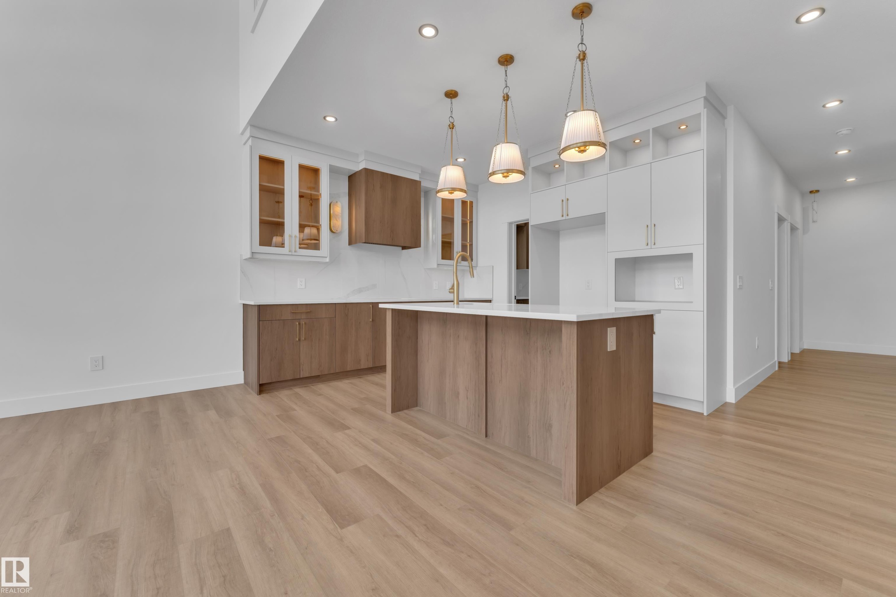 Modern kitchen featuring a central island with a white countertop, light wood-finish cabinetry, white upper cabinetry with open shelving, recessed lighting, and three pendant light fixtures - 13128 187 Avenue, Edmonton, AB - Indoor Photo Showing Kitchen