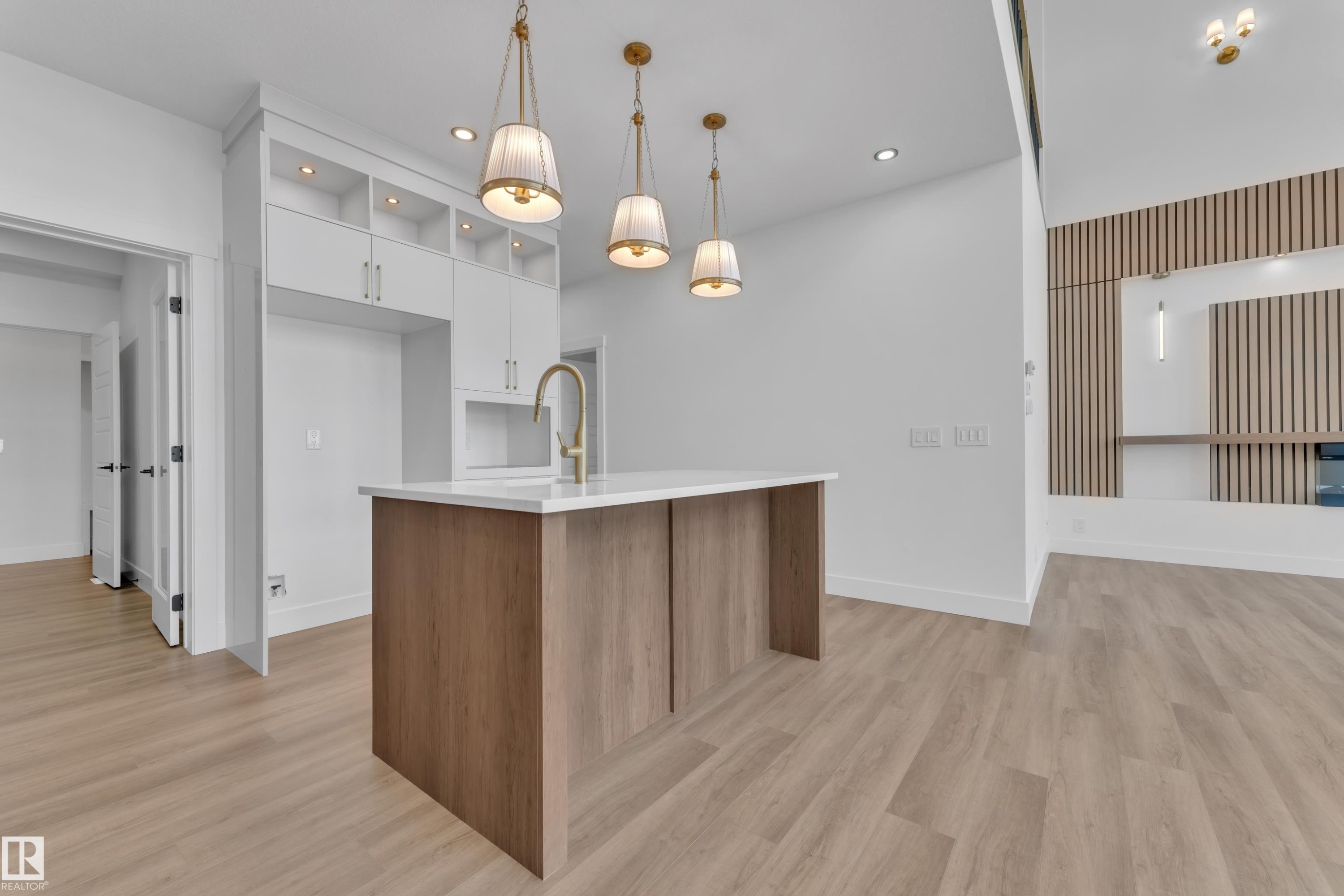 Kitchen island with a white countertop and wood-finish base, complemented by three brass-finish pendant lights - 13128 187 Avenue, Edmonton, AB - Indoor Photo Showing Kitchen
