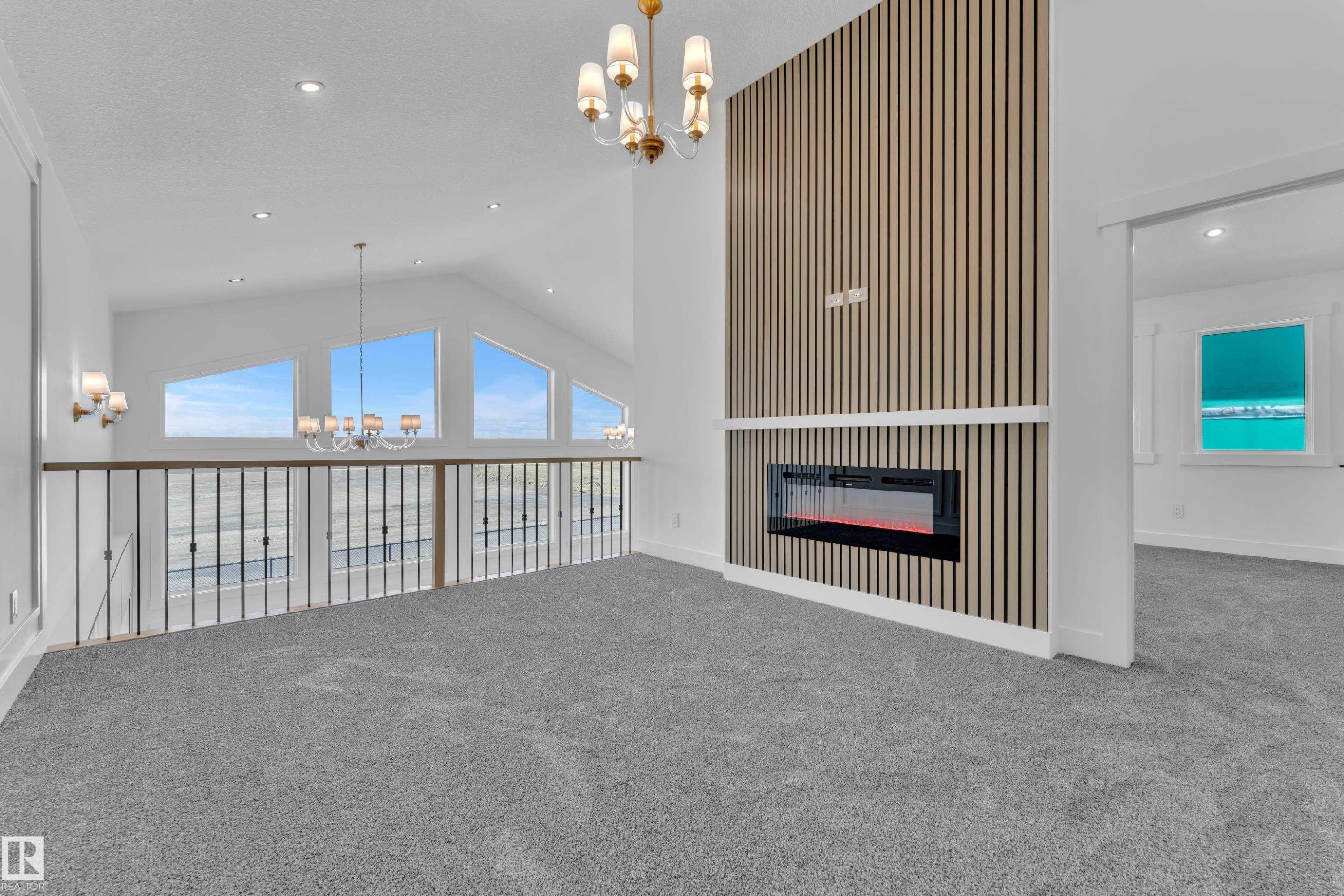 Carpeted upper-level space featuring a contemporary fireplace with a slatted wood-finish accent wall, vaulted ceilings, recessed lighting, and a chandelier - 13128 187 Avenue, Edmonton, AB - Indoor Photo Showing Other Room