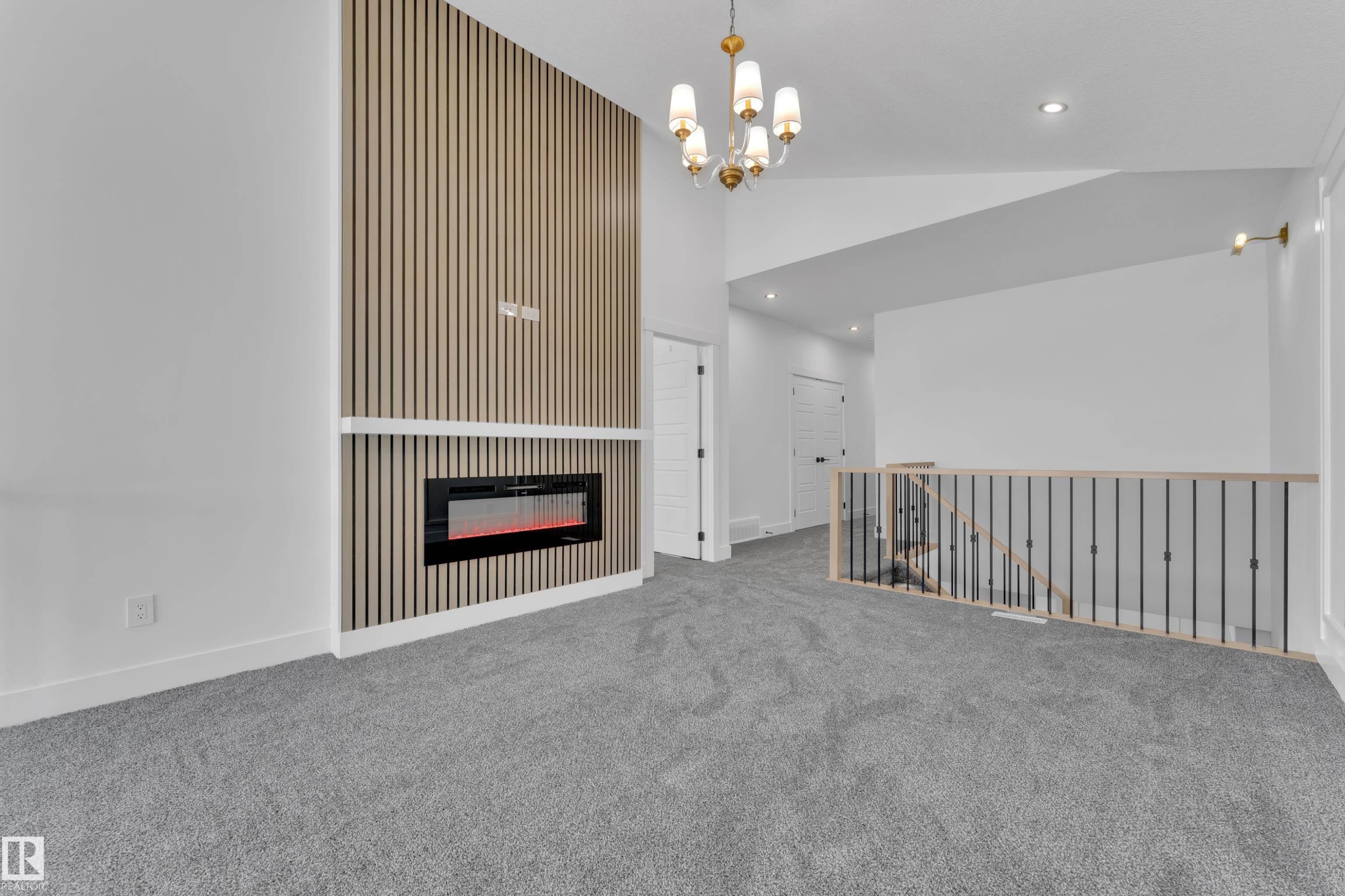 Living area featuring a floor-to-ceiling accent wall with a linear electric fireplace, grey carpeting, a gold-tone chandelier, recessed lighting, and a staircase with an open baluster design - 13128 187 Avenue, Edmonton, AB - Indoor With Fireplace