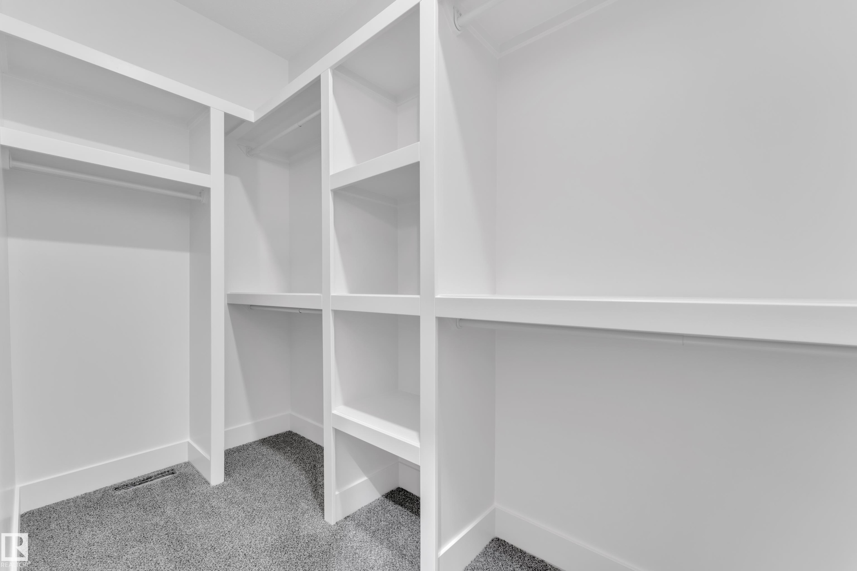 Built-in custom closet system featuring white shelving, multiple hanging rods, and grey carpeting - 13128 187 Avenue, Edmonton, AB - Indoor With Storage