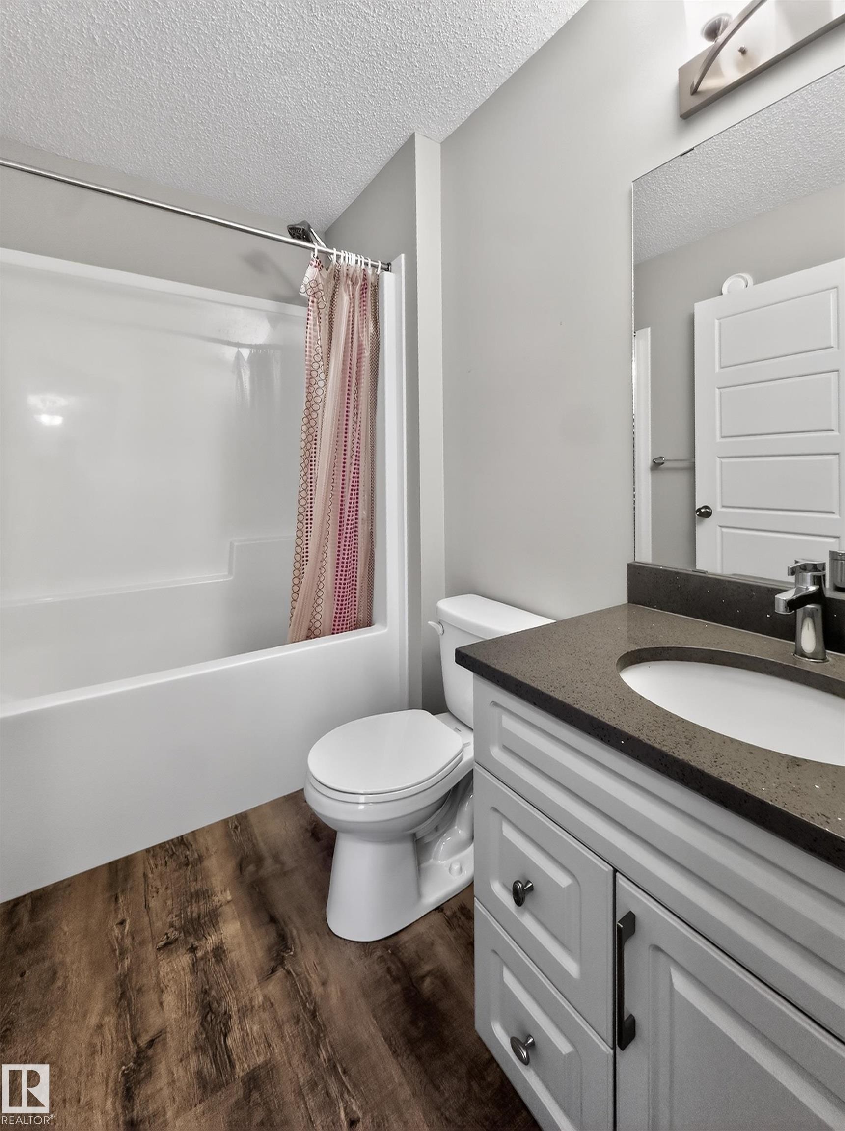 The bathroom features a white tub and shower combination, a white toilet, and a vanity with a dark countertop and white cabinetry - 15 2072 Wonnacott Way, Edmonton, AB - Indoor Photo Showing Bathroom