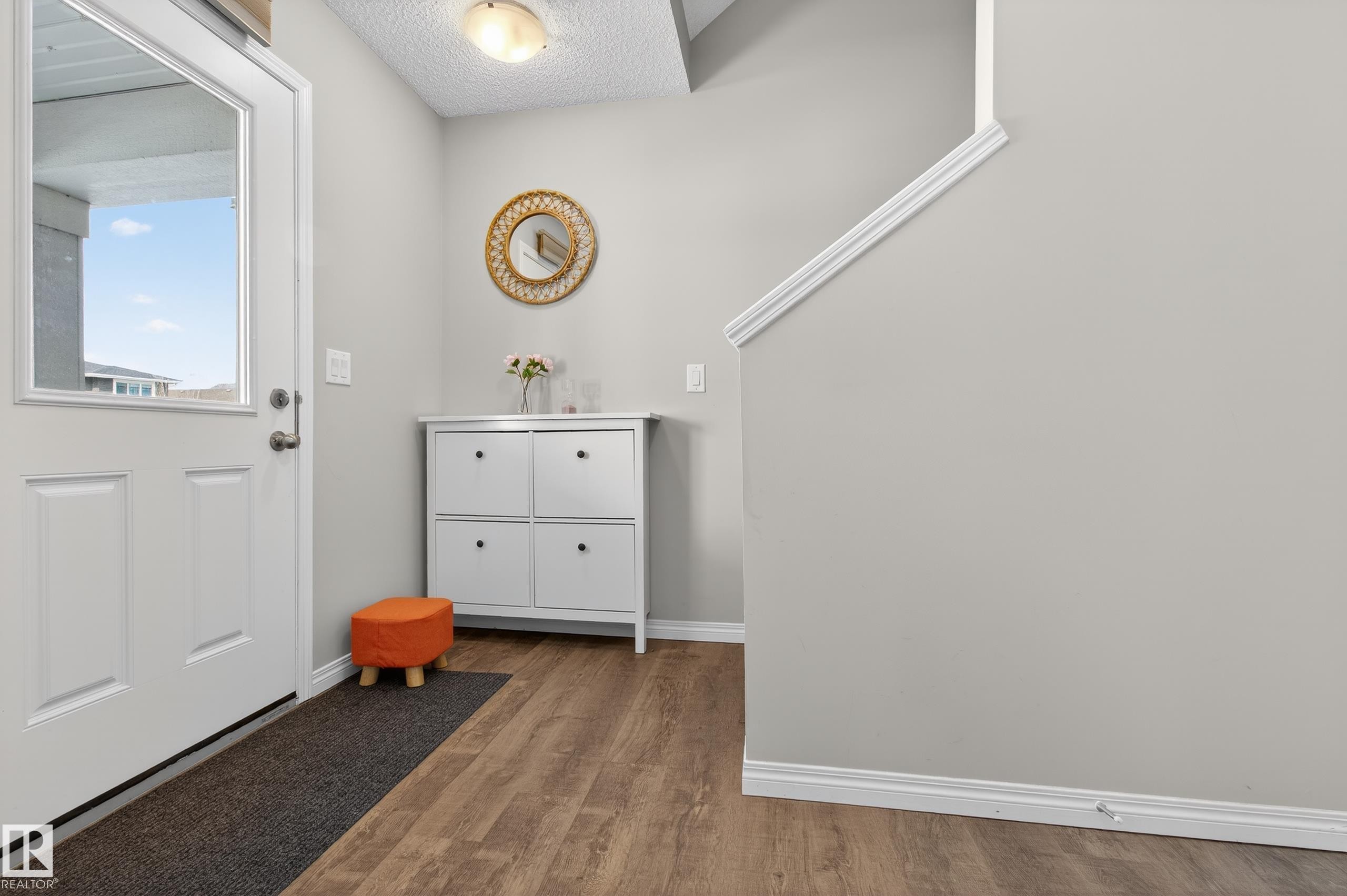 The entryway features a white front door with a window, wood-style flooring, and light gray walls - 15 2072 Wonnacott Way, Edmonton, AB - Indoor Photo Showing Other Room