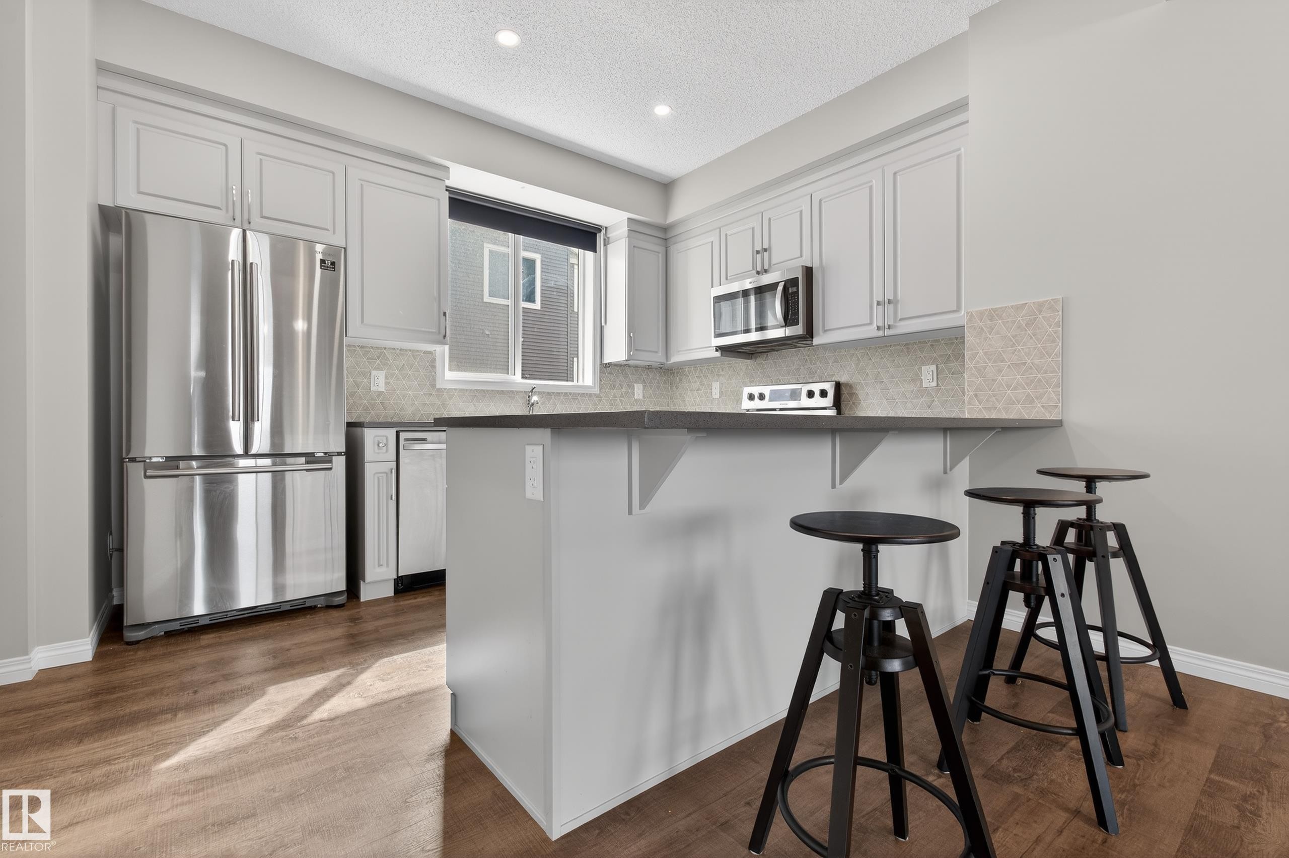 The kitchen features light grey cabinetry, stainless steel appliances, a window above the sink, and dark countertops - 15 2072 Wonnacott Way, Edmonton, AB - Indoor Photo Showing Kitchen With Stainless Steel Kitchen With Upgraded Kitchen