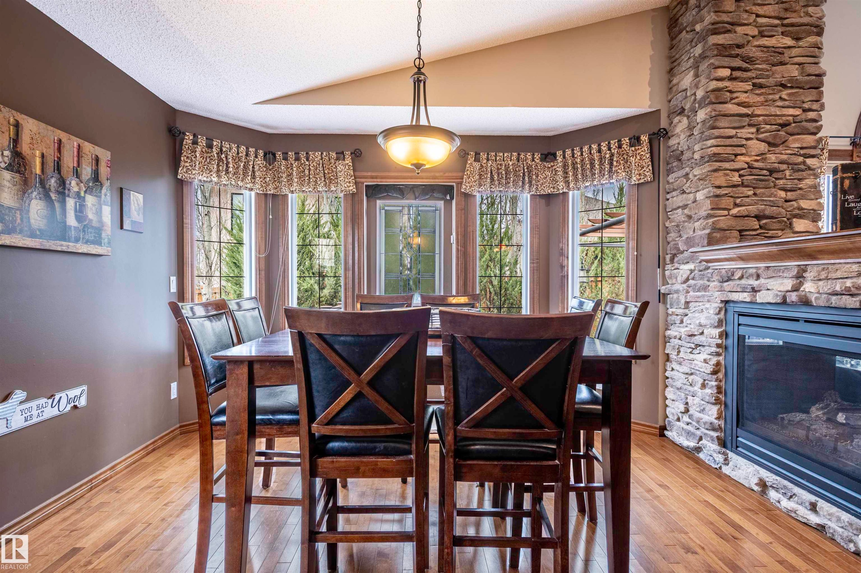 Dining area featuring a bay window, hardwood flooring, a stone-clad fireplace with a hearth, and a pendant light fixture - 19 Newton Place, St. Albert, AB - Indoor Photo Showing Dining Room With Fireplace