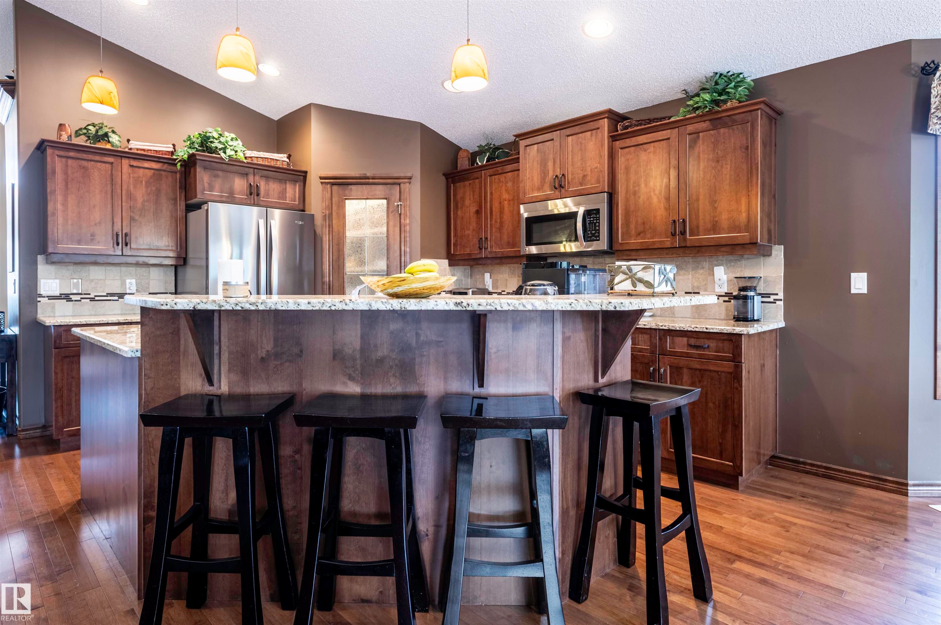Kitchen featuring wood-finish flooring, a tiered island with a stone-finish countertop, and rich wood cabinetry - 19 Newton Place, St. Albert, AB - Indoor Photo Showing Kitchen With Upgraded Kitchen