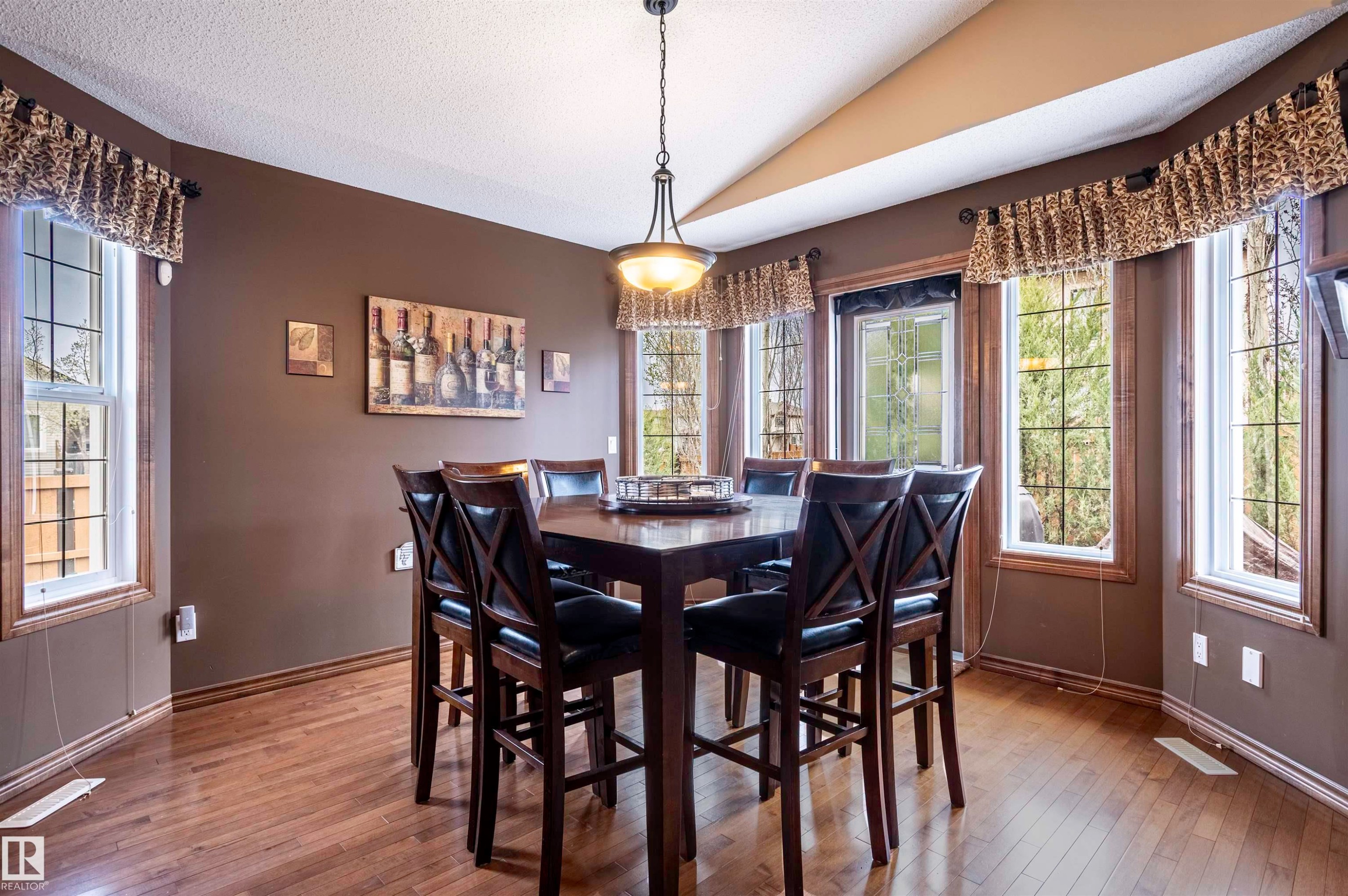 Dining area featuring wood-finish flooring, ample natural light from multiple windows, brown painted walls, a vaulted ceiling, and a hanging light fixture - 19 Newton Place, St. Albert, AB - Indoor Photo Showing Dining Room