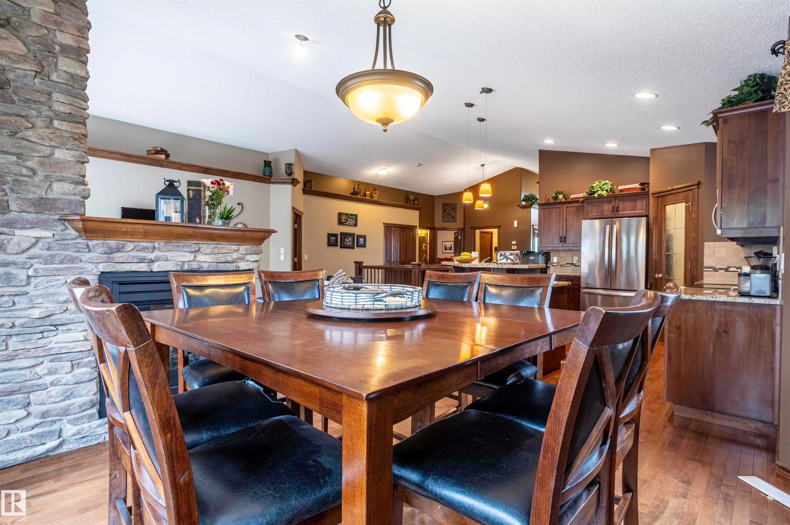 Open-concept living area featuring a stone fireplace, wood-finish flooring, and a kitchen with stainless steel appliances, granite countertops, and dark wood cabinetry - 19 Newton Place, St. Albert, AB - Indoor