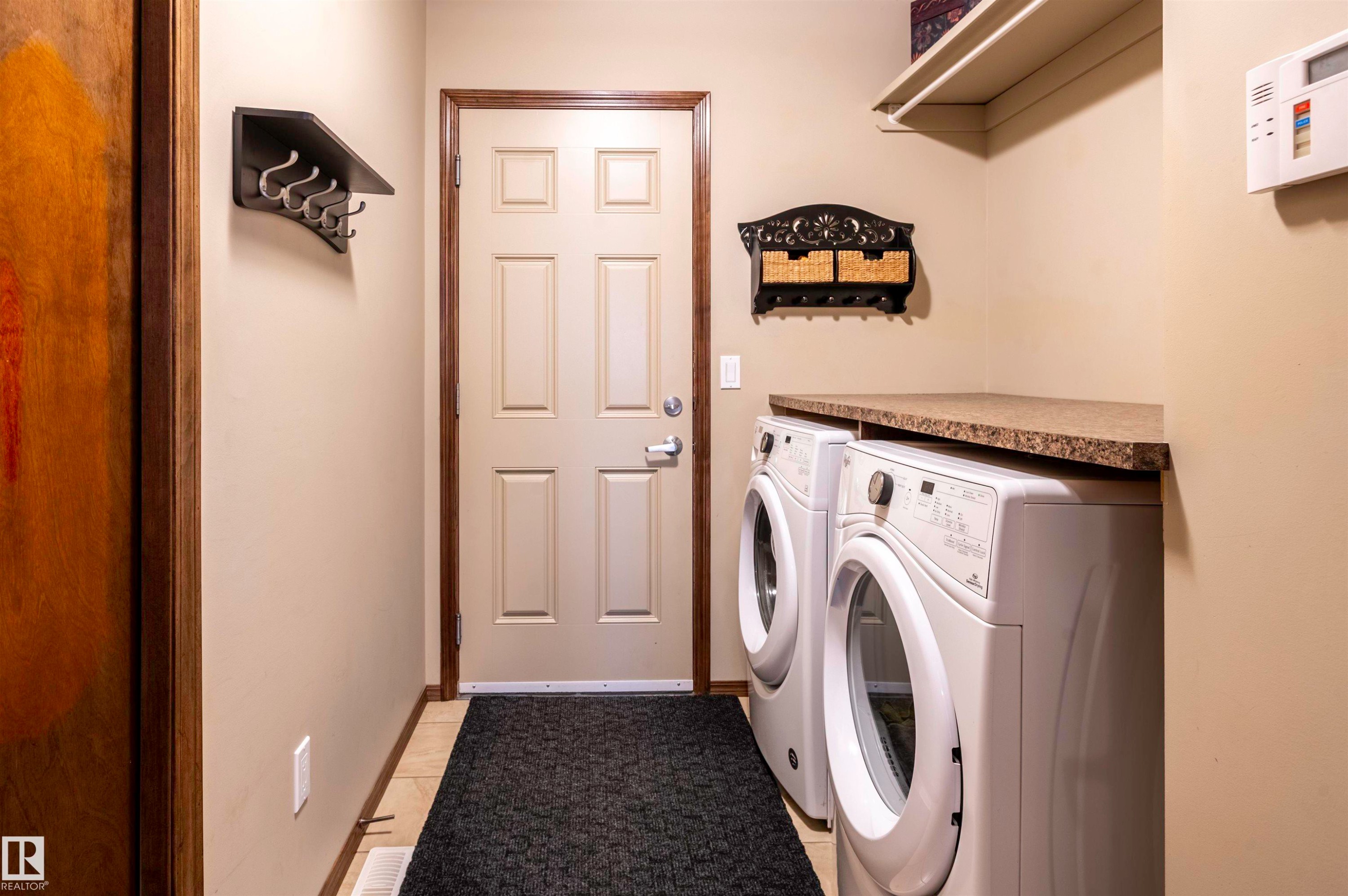 Dedicated laundry area featuring a front-loading washer and dryer, speckled countertop, and built-in shelving - 19 Newton Place, St. Albert, AB - Indoor Photo Showing Laundry Room
